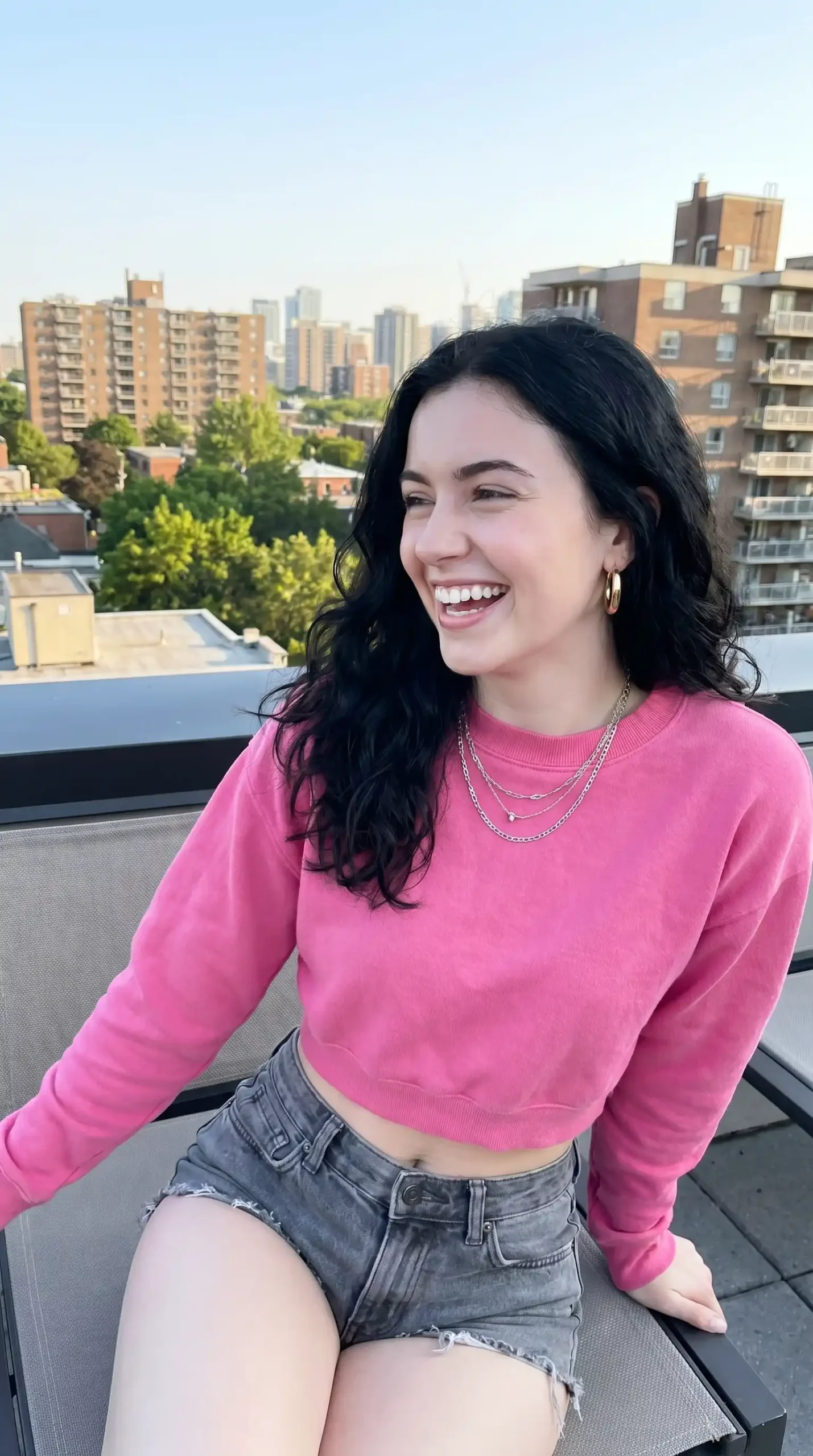 Woman wearing hot pink crop crewneck sweatshirt with grey denim cutoff shorts outdoors