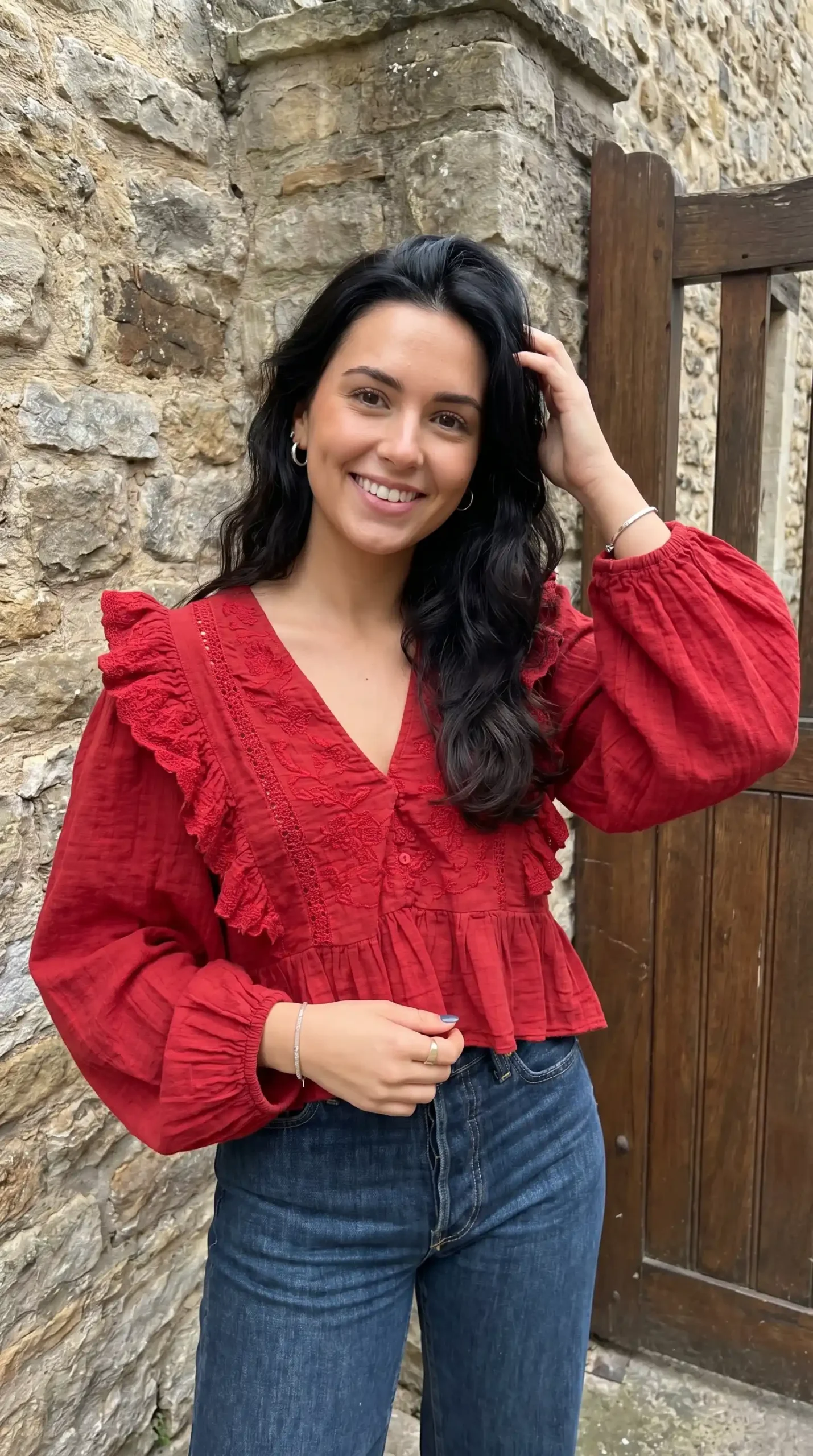 Woman wearing red embroidered ruffle V-neck peplum blouse with dark blue jeans outdoors