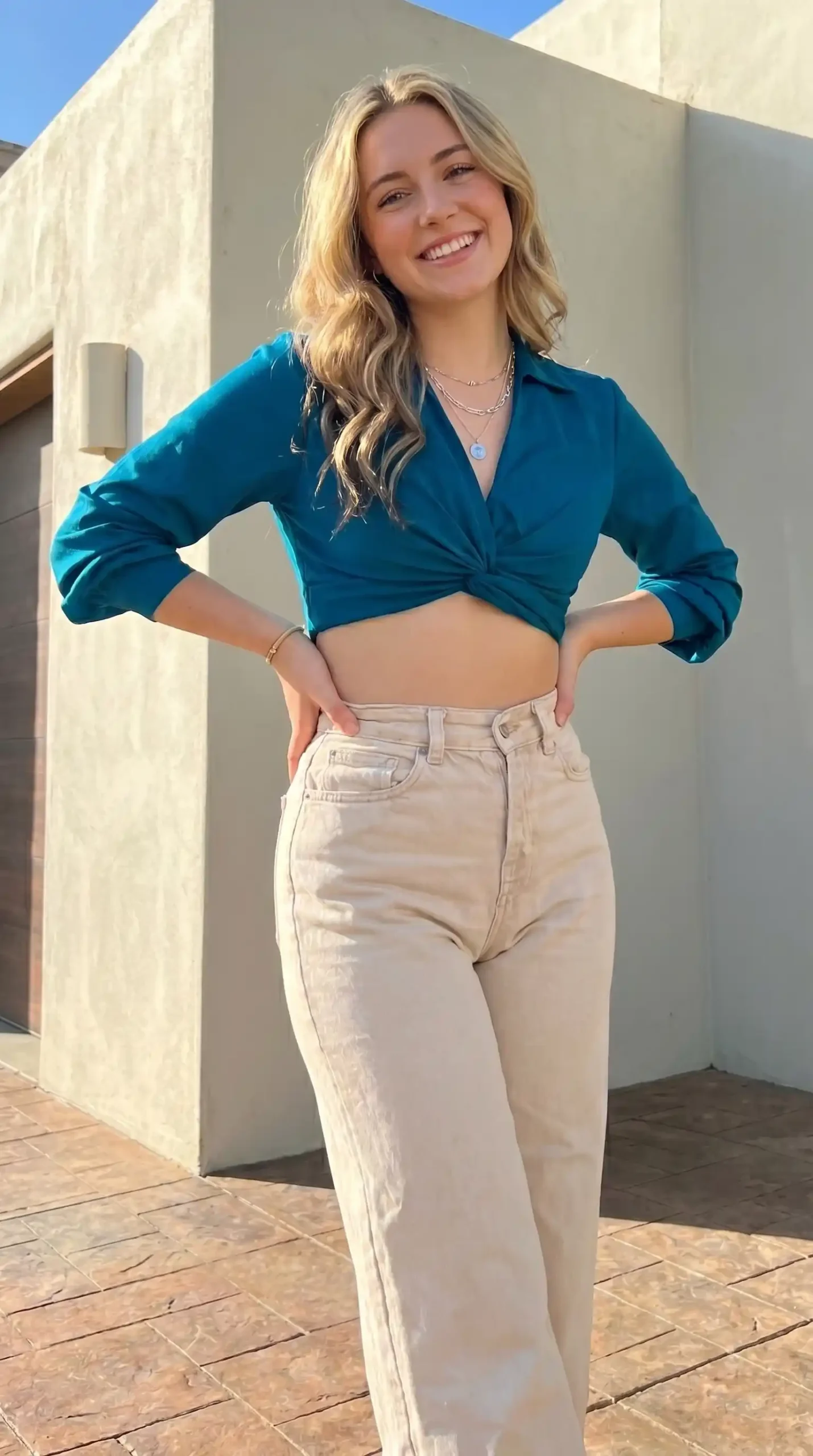 Woman wearing teal twist-front crop shirt with beige wide-leg jeans outdoors