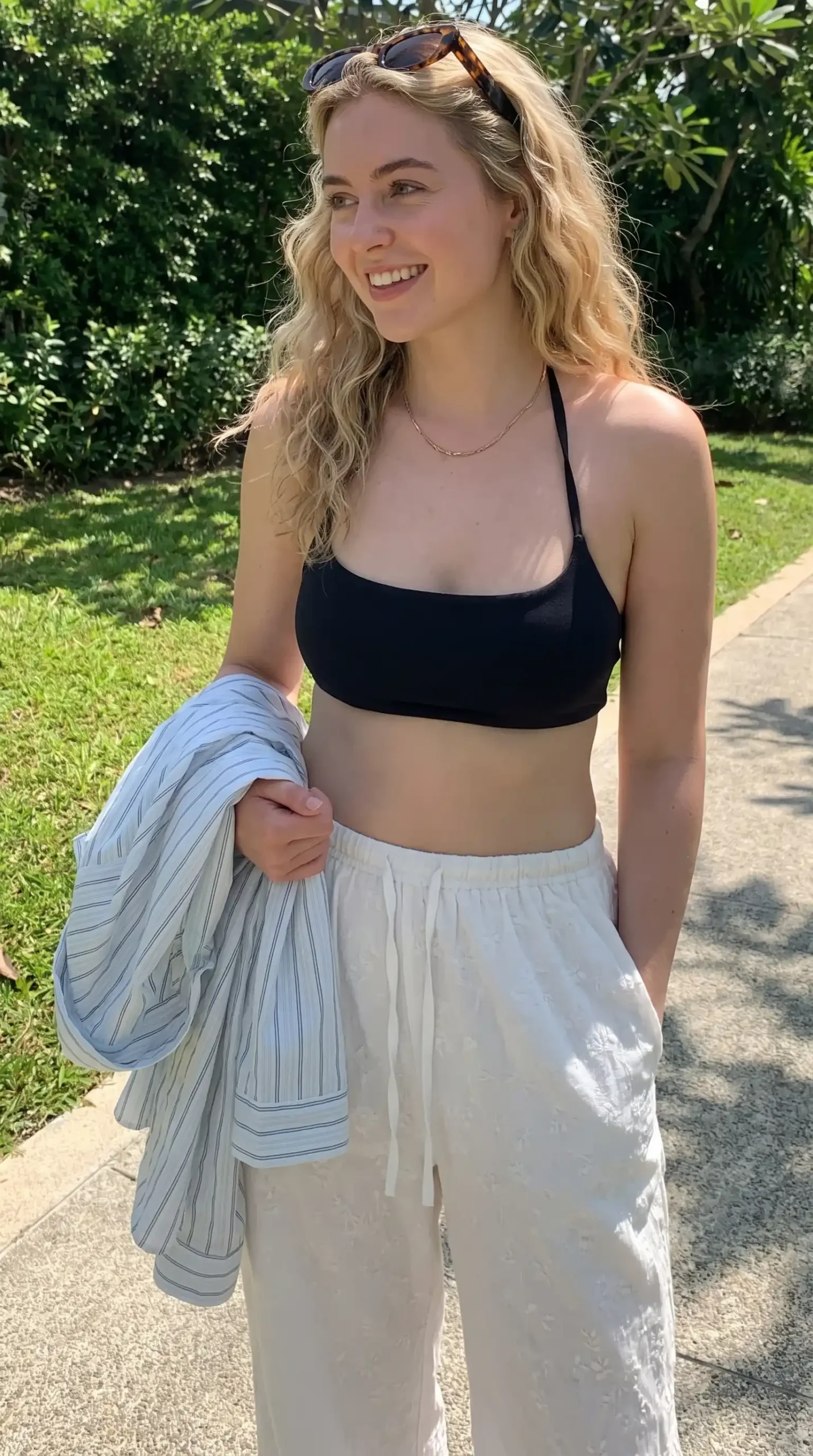 Woman wearing black halter bralette top with cream textured wide-leg pants and striped shirt outdoors
