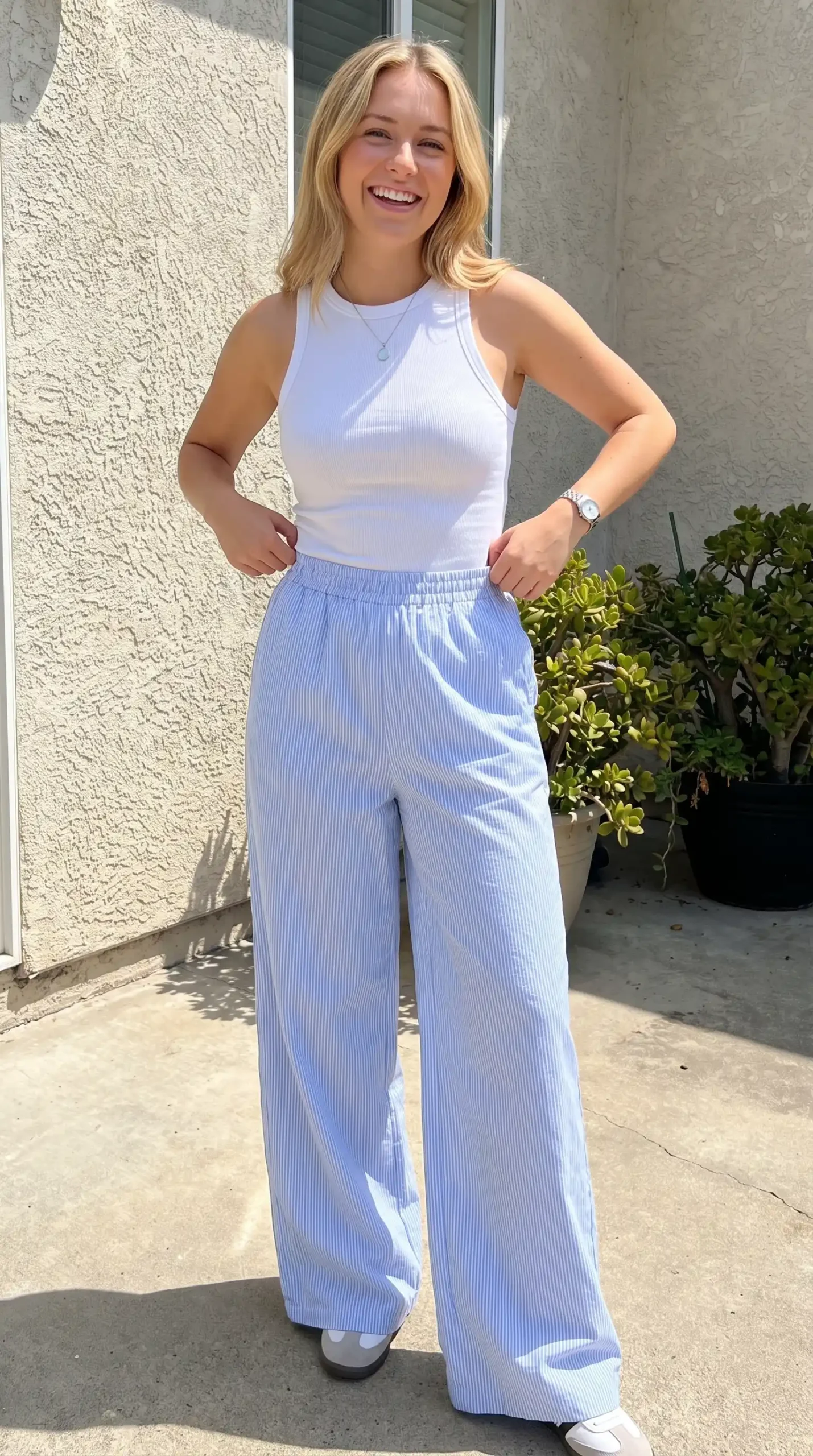 Woman wearing white ribbed racerback tank top with blue and white striped wide-leg pants outdoors