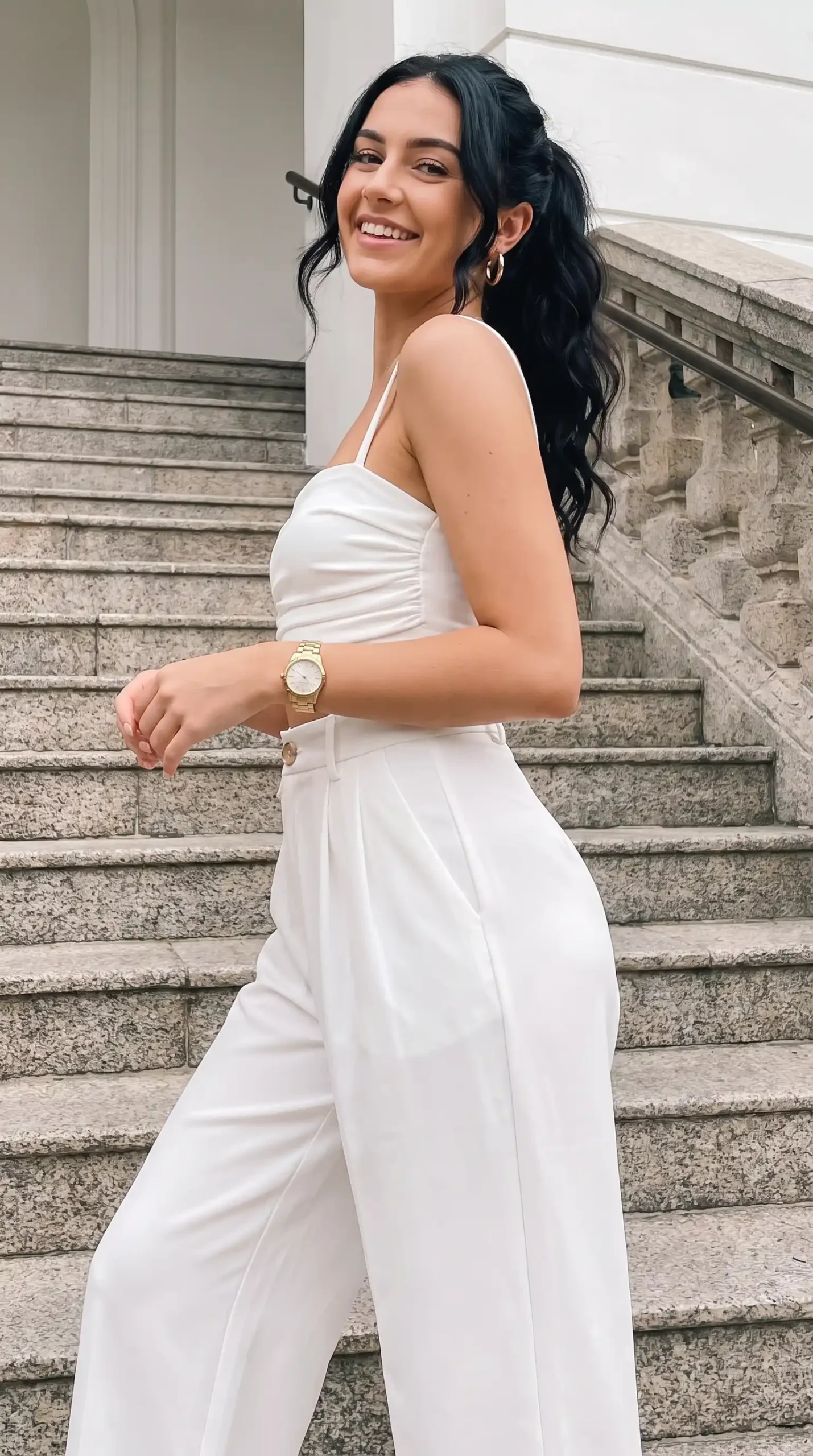 Woman wearing white ruched spaghetti strap crop top with white tailored wide-leg trousers outdoors