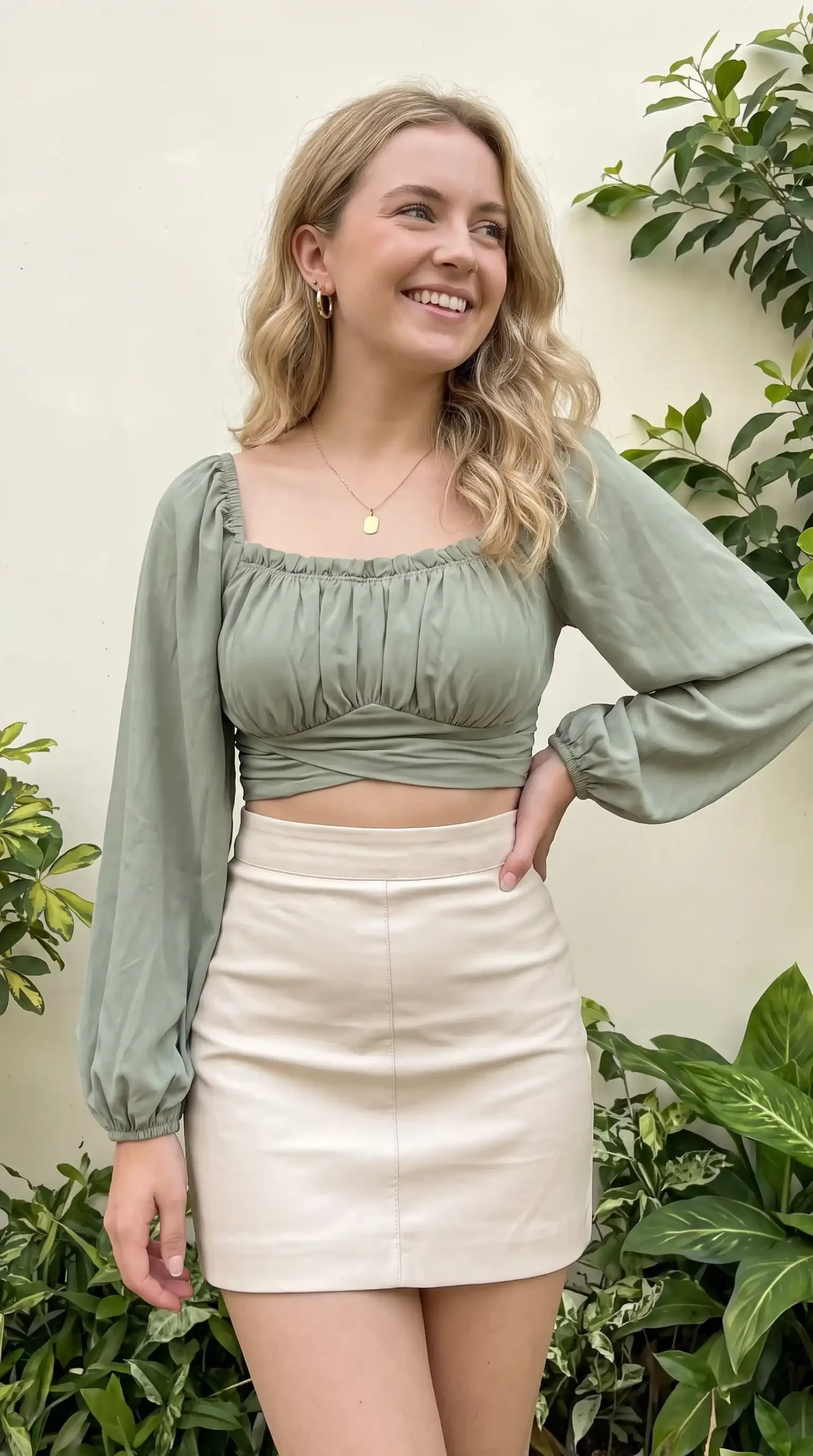 Woman wearing sage green wrap crop top with cream leather mini skirt outdoors