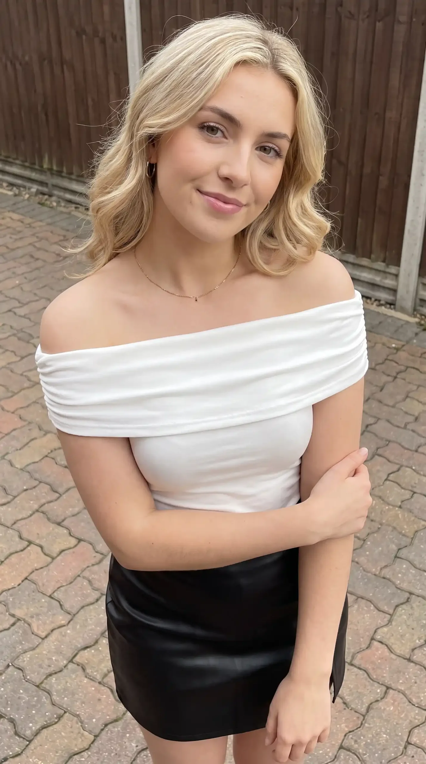 Woman wearing white off shoulder bandeau top with black faux leather mini skirt outdoors