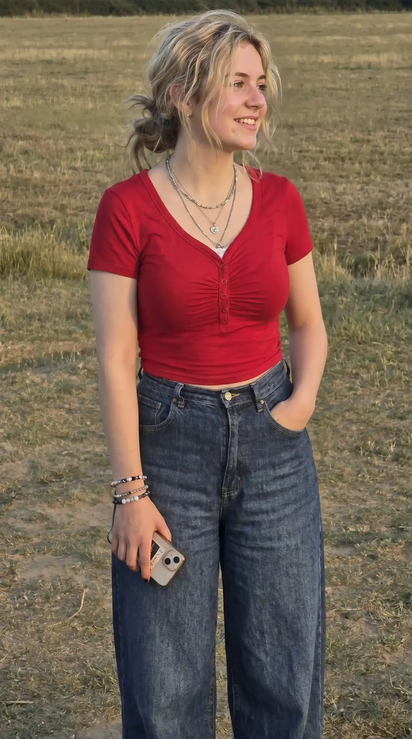 Woman wearing red ruched henley top with dark wide-leg jeans outdoors at sunset