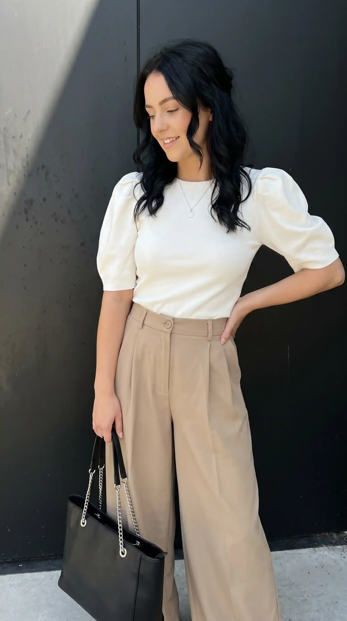 Woman wearing white puff sleeve top with beige pleated trousers and black tote bag