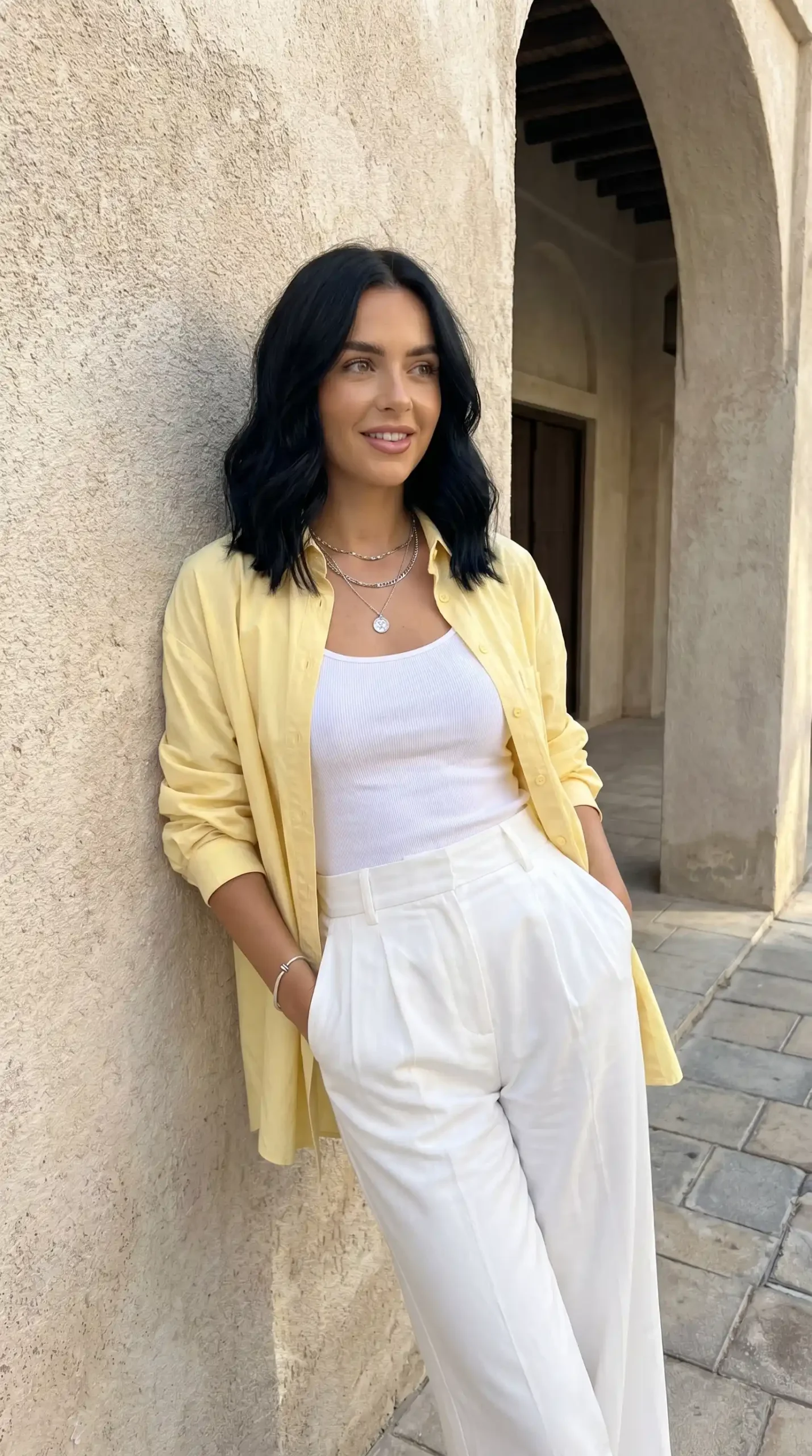 Woman wearing yellow oversized shirt over white tank top with white trousers outdoors