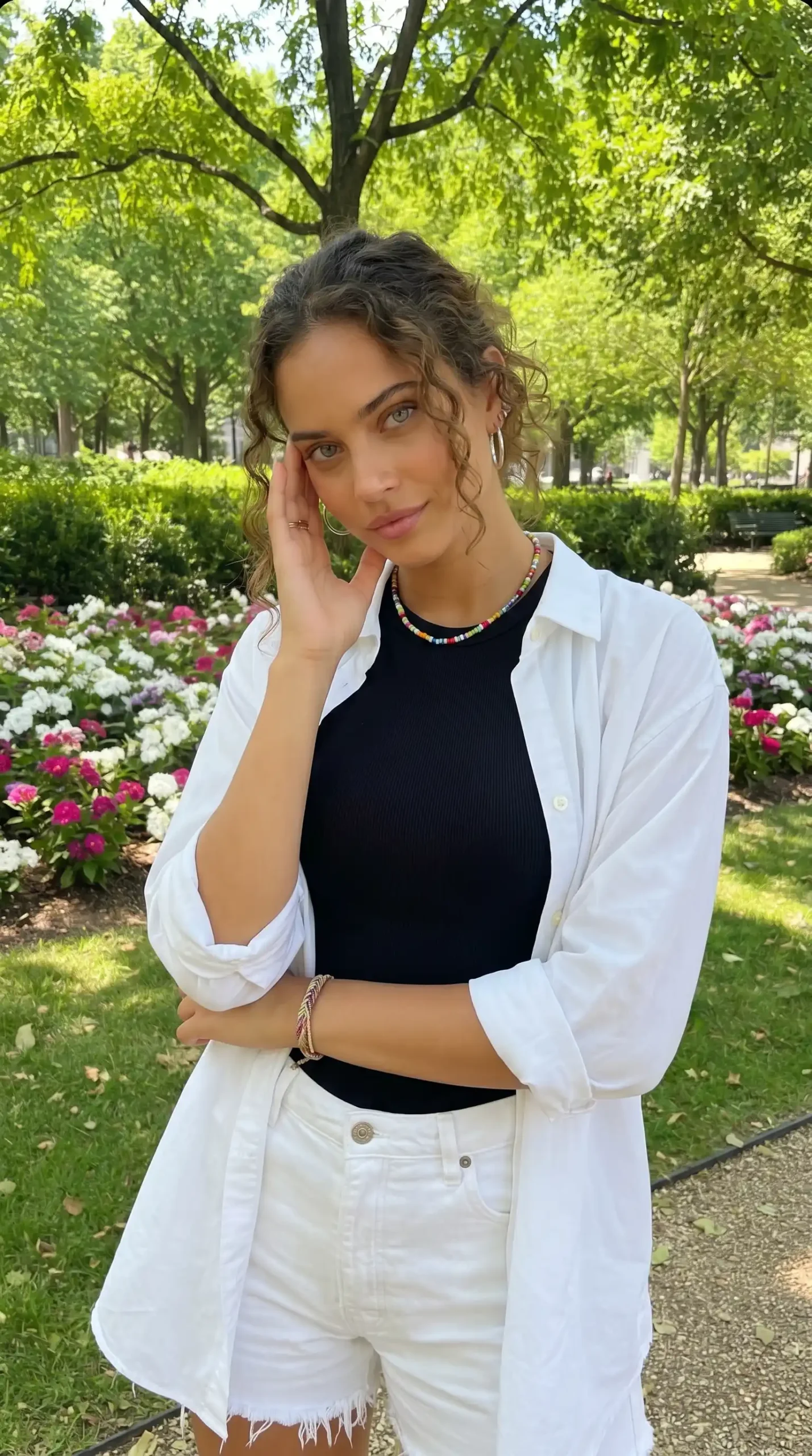 Woman wearing black ribbed tank top with white oversized shirt and white denim shorts in park