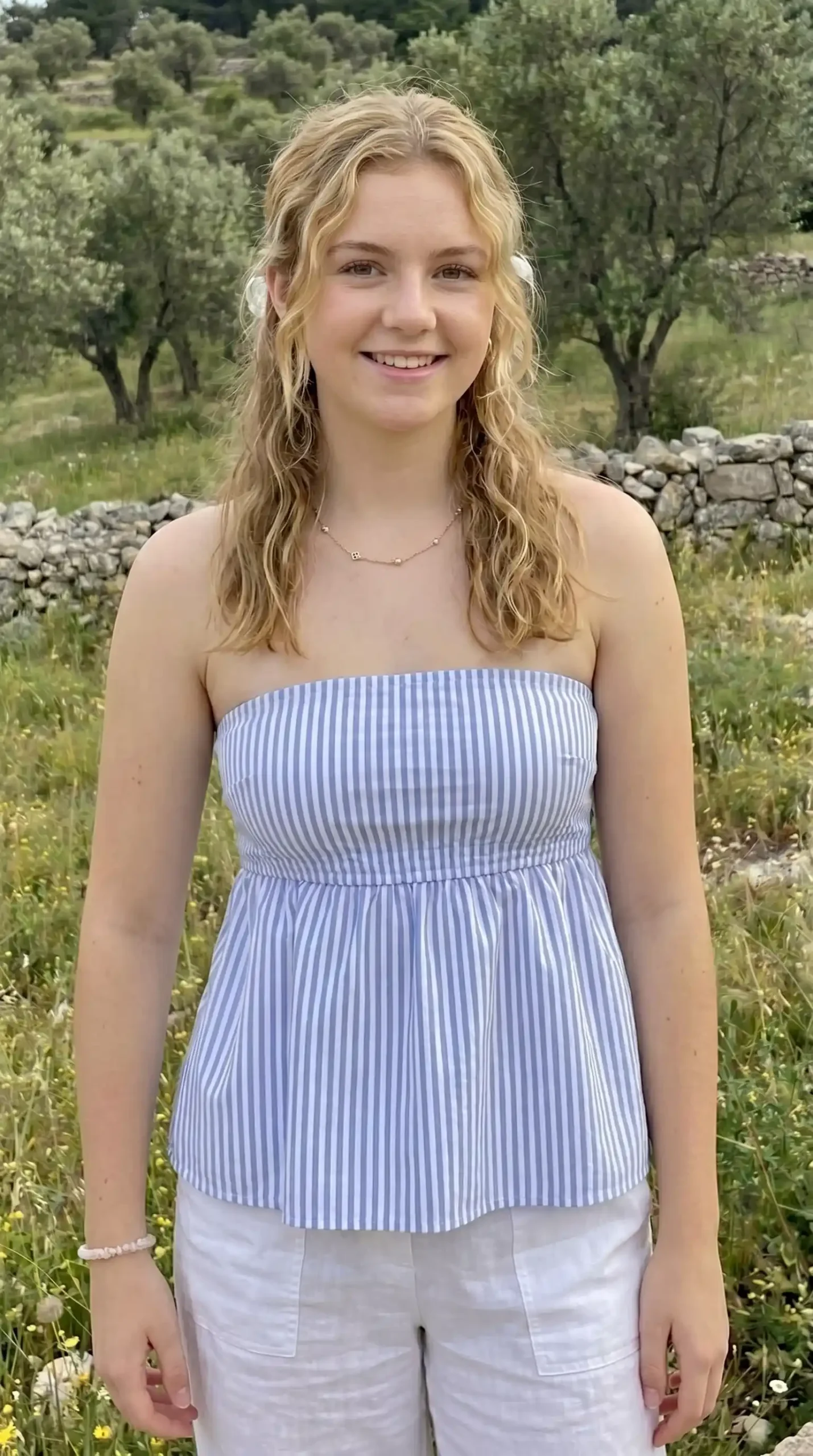 Woman wearing blue and white striped tube babydoll top with white pants in countryside