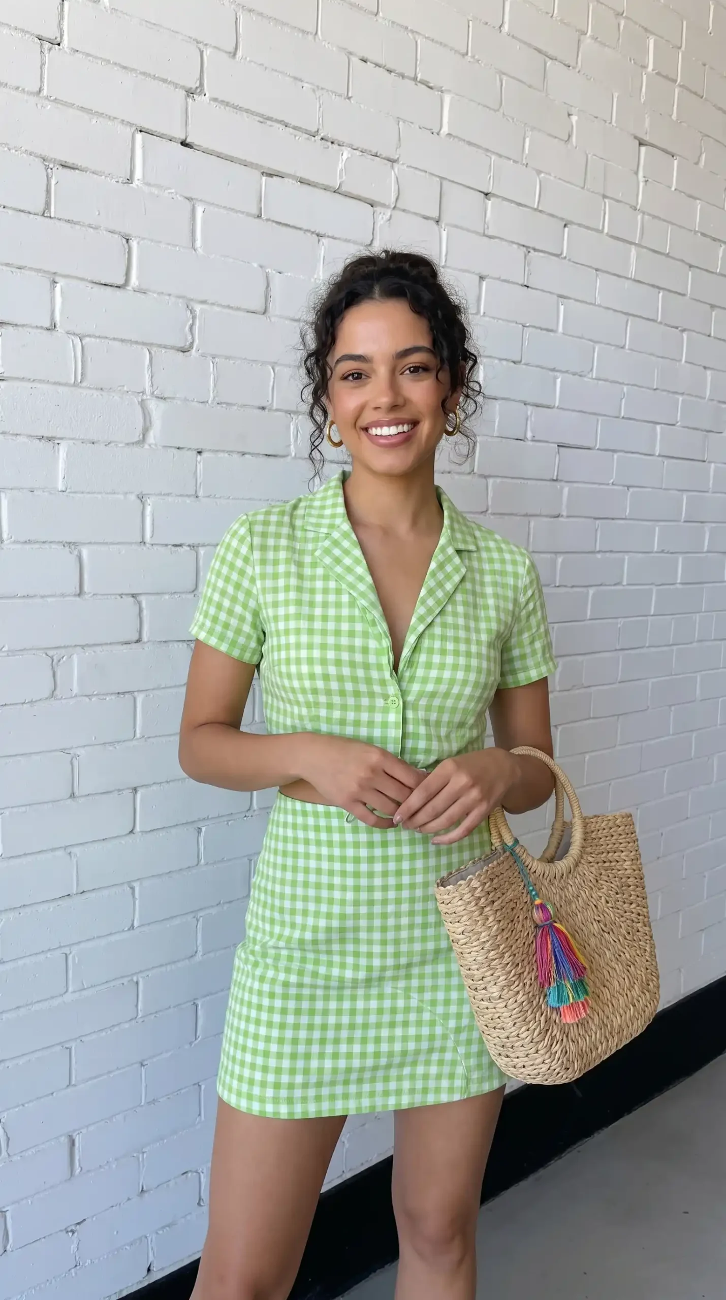 Woman wearing green and white gingham co-ord crop shirt and mini skirt with woven tote bag