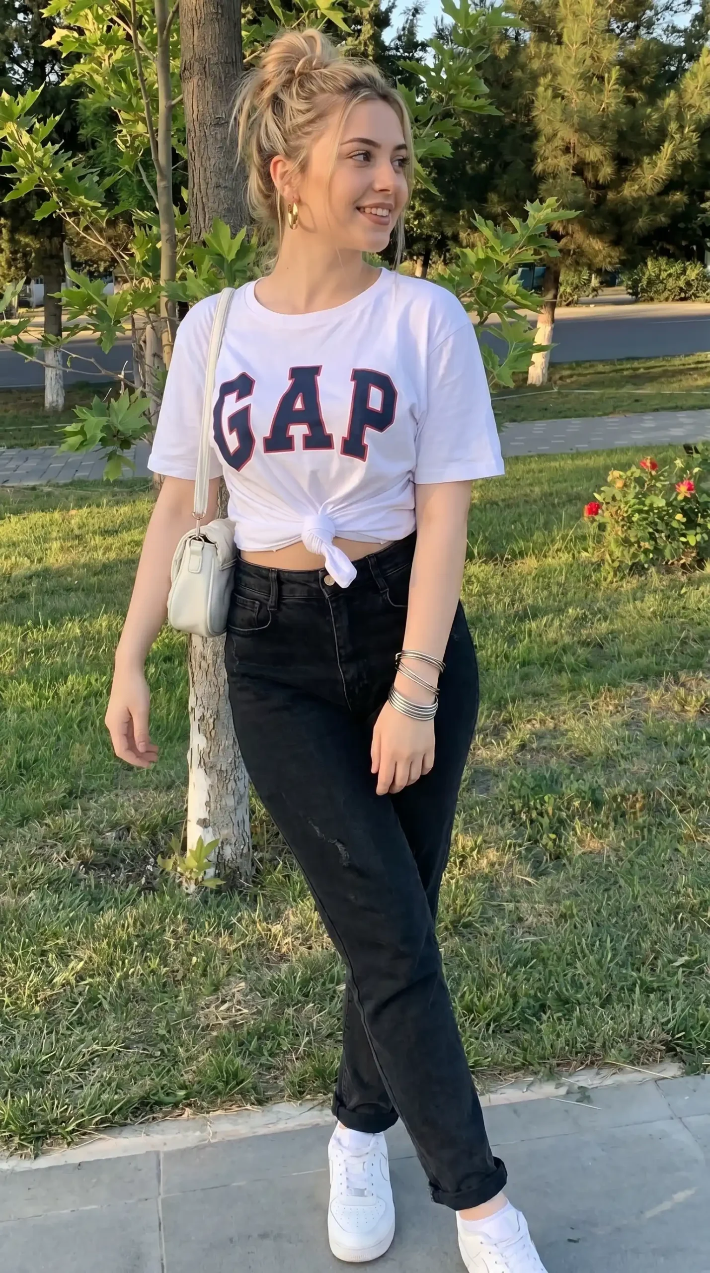 Woman wearing white knotted graphic tee with black jeans and white sneakers outdoors