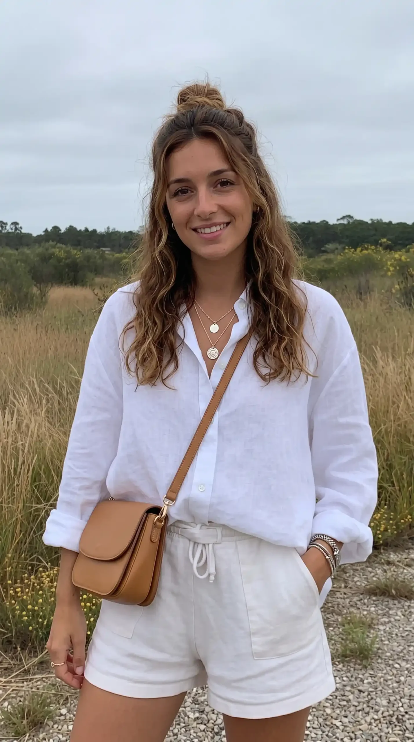 Woman wearing white linen oversized shirt with white linen shorts and tan crossbody bag outdoors