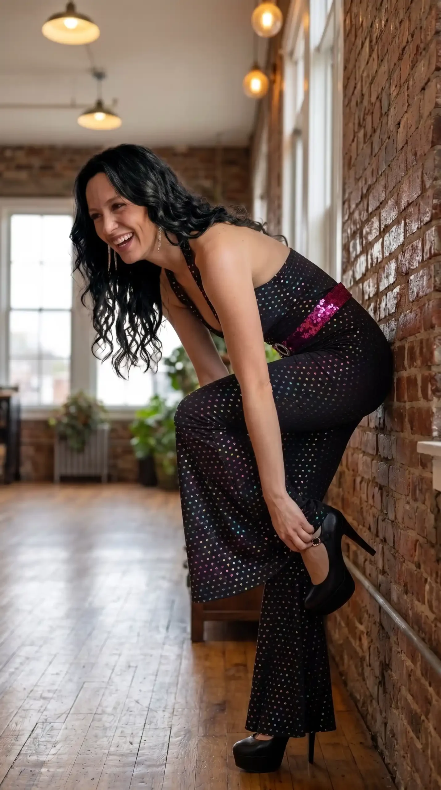 Woman dressed in 1970s disco style black holographic dot print halter neck flared maxi jumpsuit