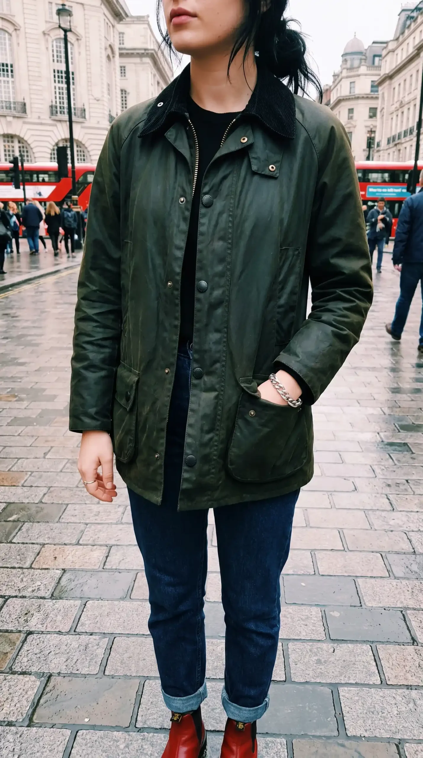 Woman wearing olive green wax jacket with dark wash jeans black top and red ankle boots on London street