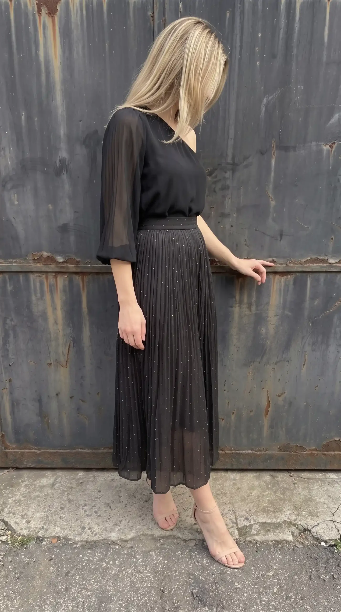 Woman in black sheer chiffon flared sleeve blouse with black sparkle pleated midi skirt and nude heels