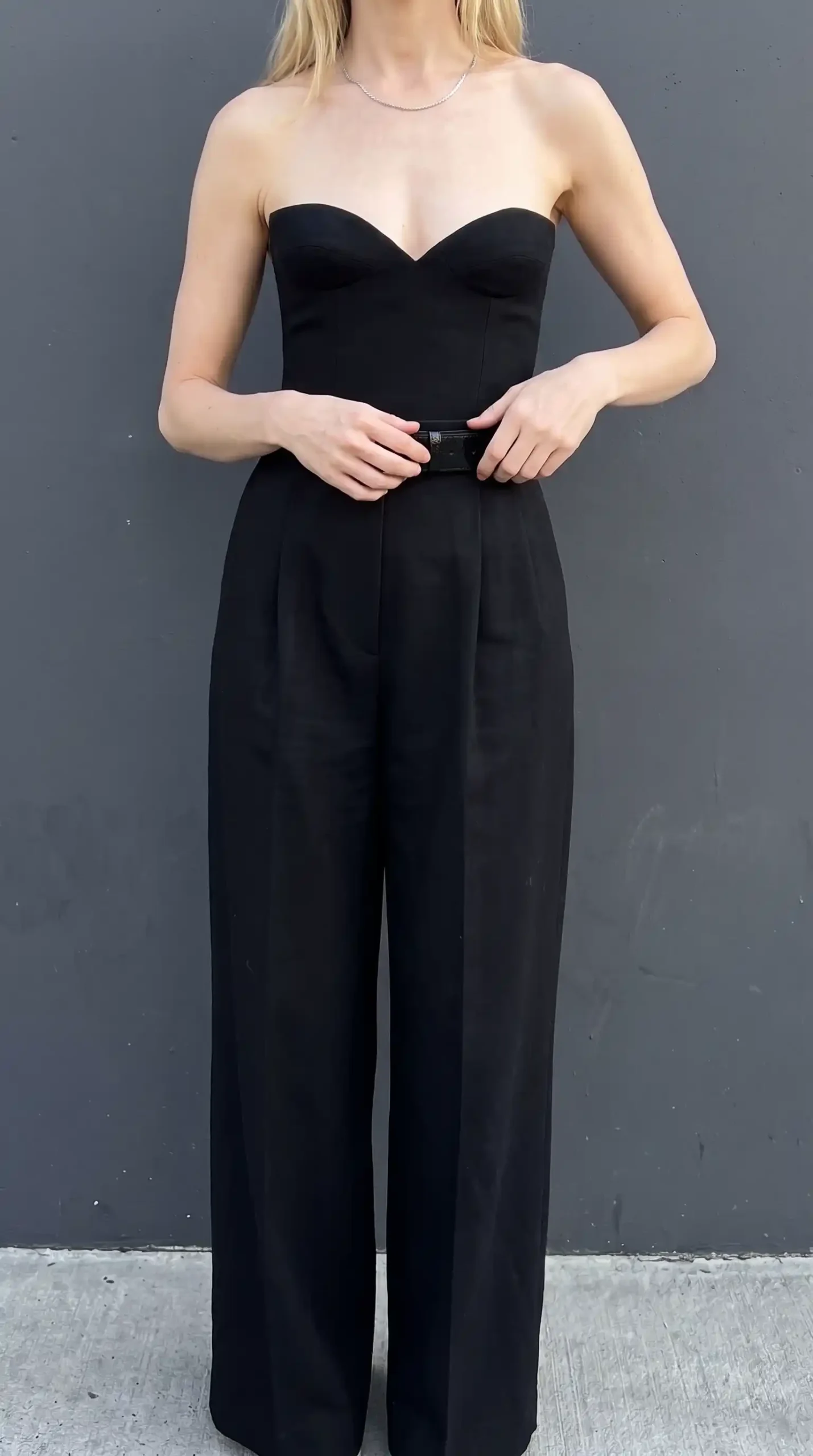 Woman in black sweetheart strapless corset with black wide leg tailored trousers and black belt
