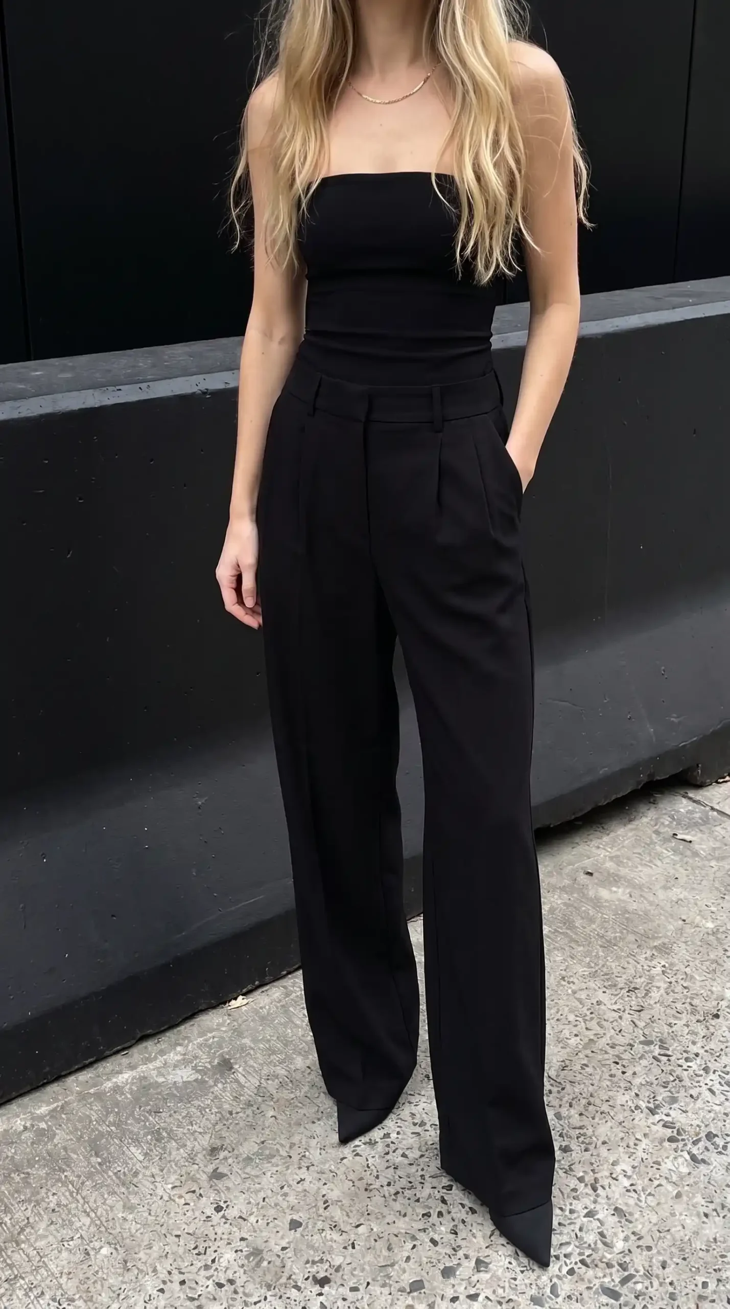 Woman in black strapless tube top with black high waist wide leg tailored trousers and pointed heels