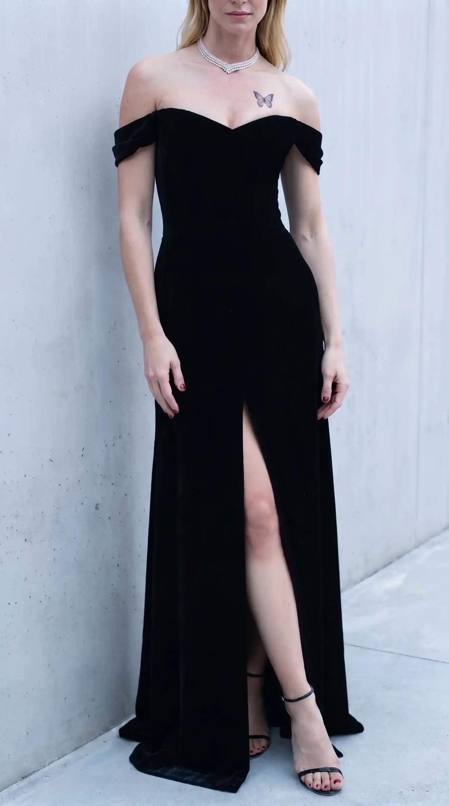 Woman in black velvet off shoulder sweetheart corset gown with front slit and black strappy heeled sandals