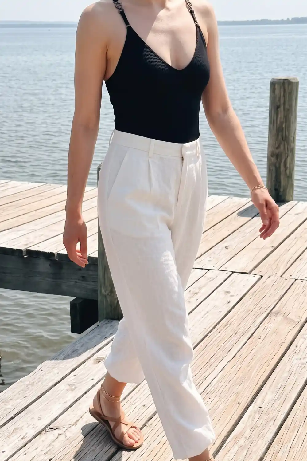 Woman in black chain strap bodysuit with white linen wide leg trousers on wooden dock