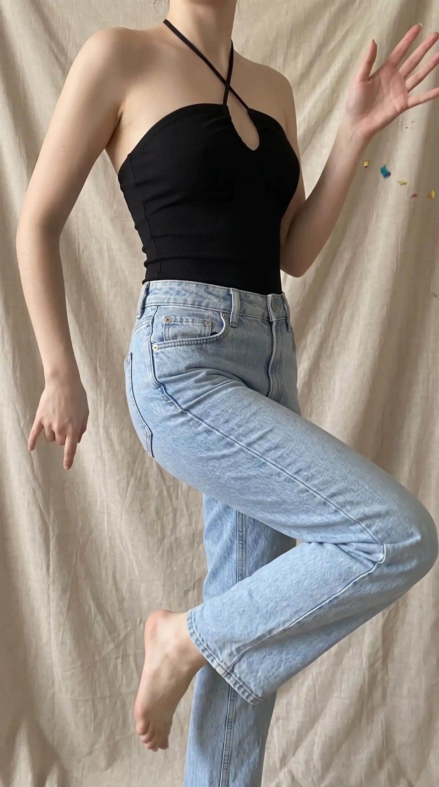 Woman wearing black ribbed crossover halter neck cutout crop top with light wash straight leg jeans