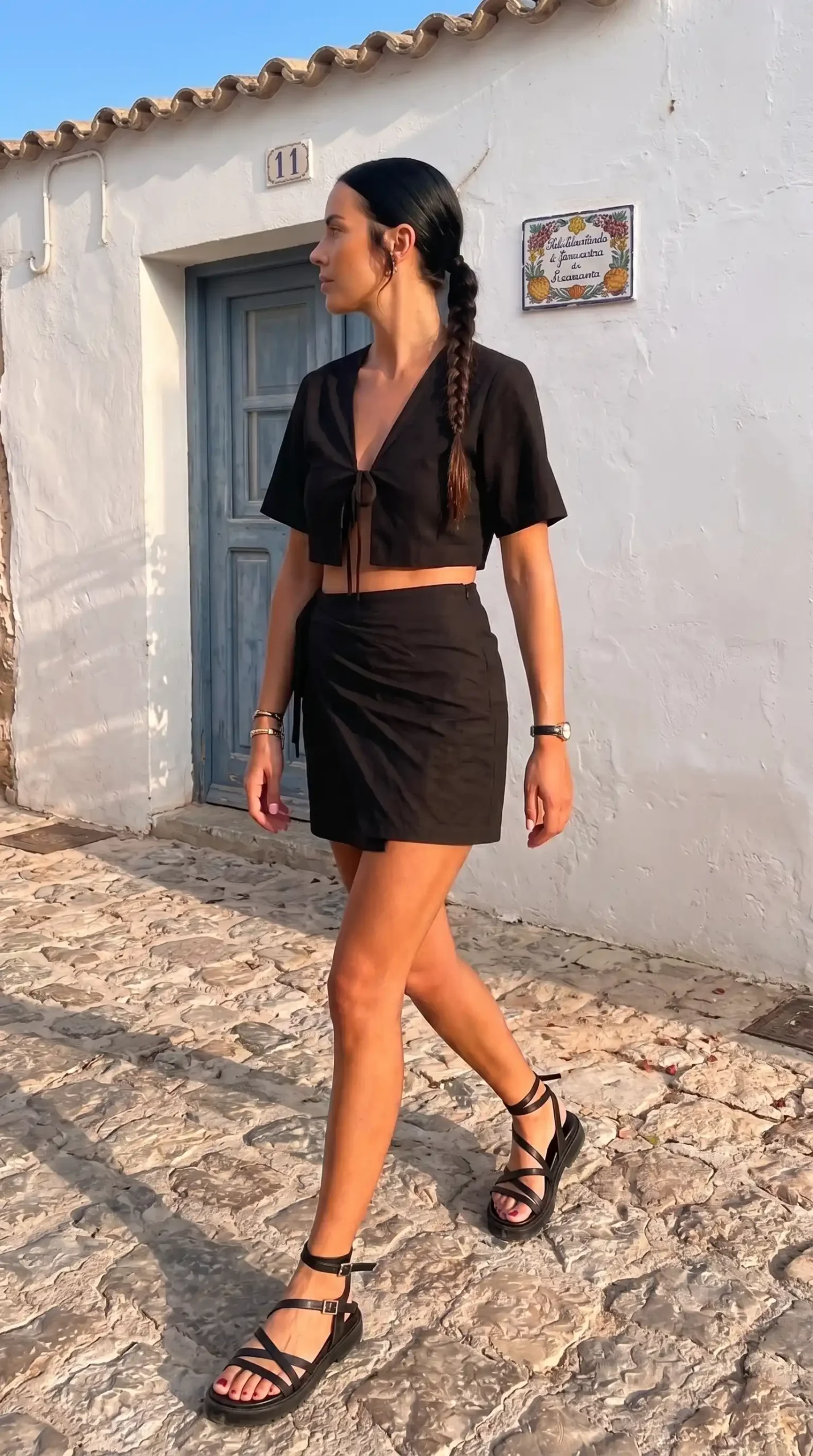 Woman wearing black linen tie-front crop top and mini skirt on European cobblestone street