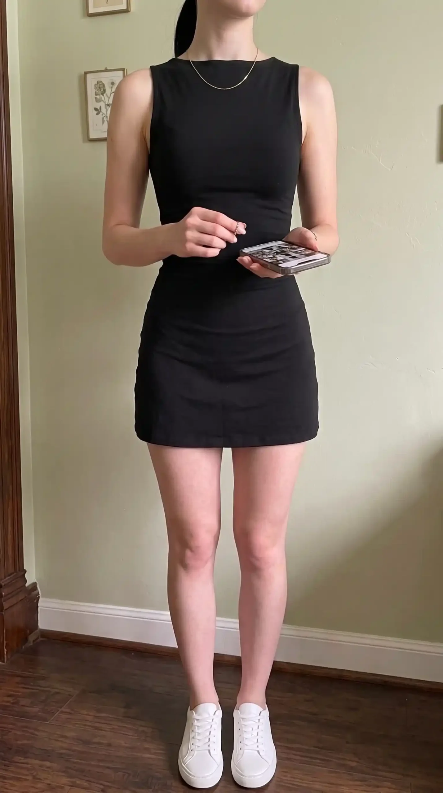 Black sleeveless ruched bodycon mini dress with white sneakers indoors