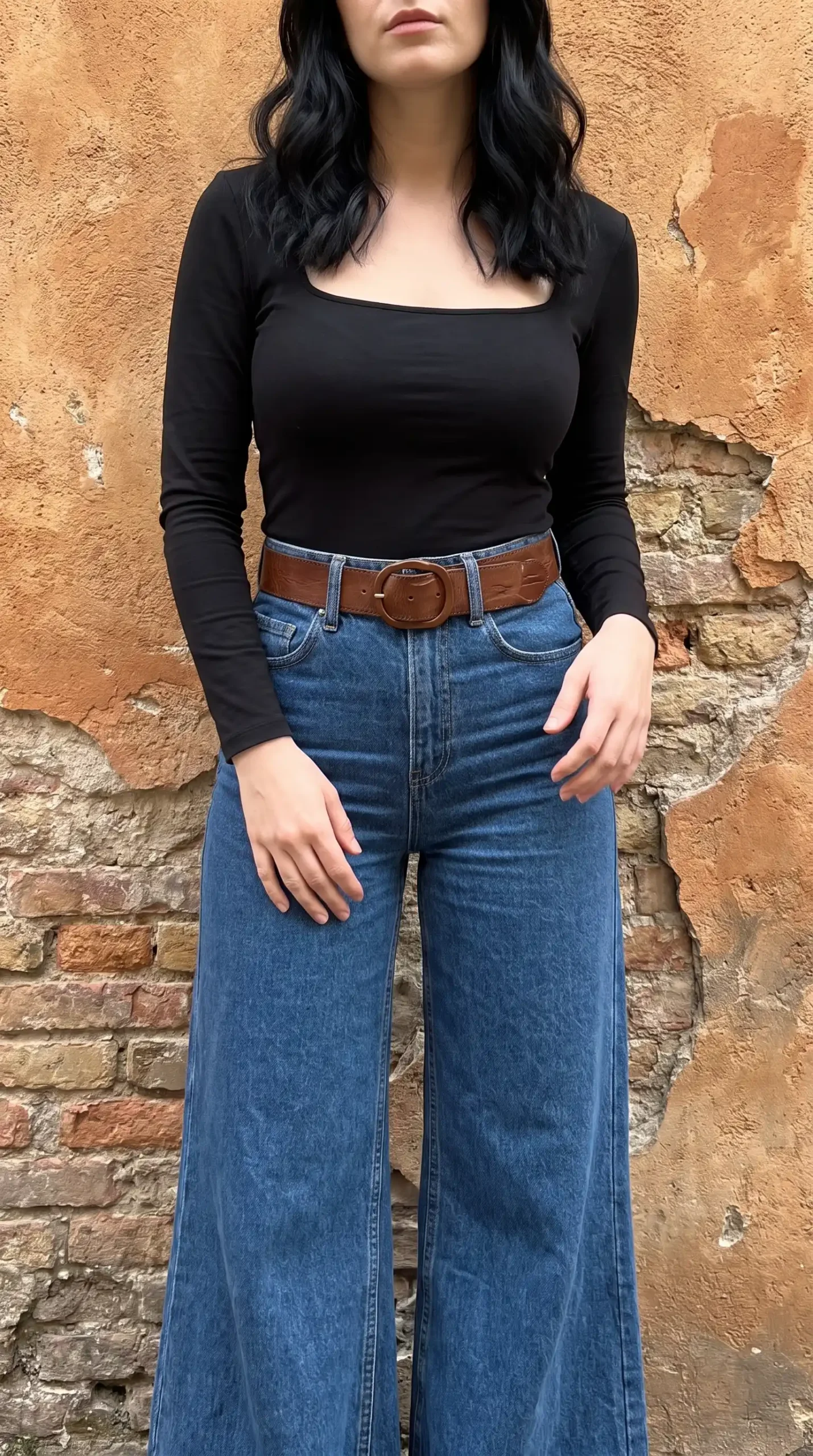 Woman wearing black square neck long sleeve top with wide leg jeans and brown belt