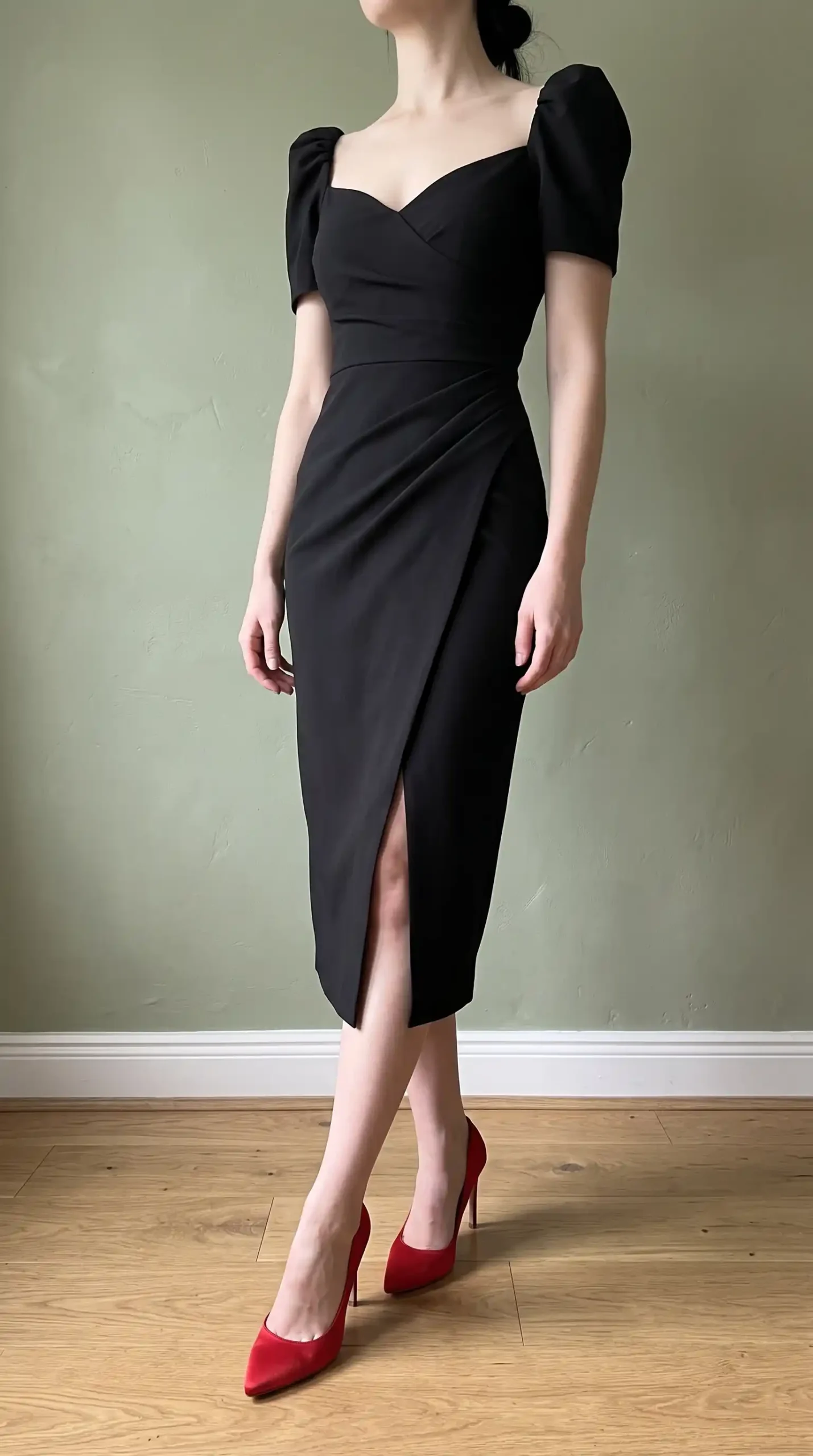 Woman wearing black sweetheart puff sleeve ruched wrap midi dress with front slit