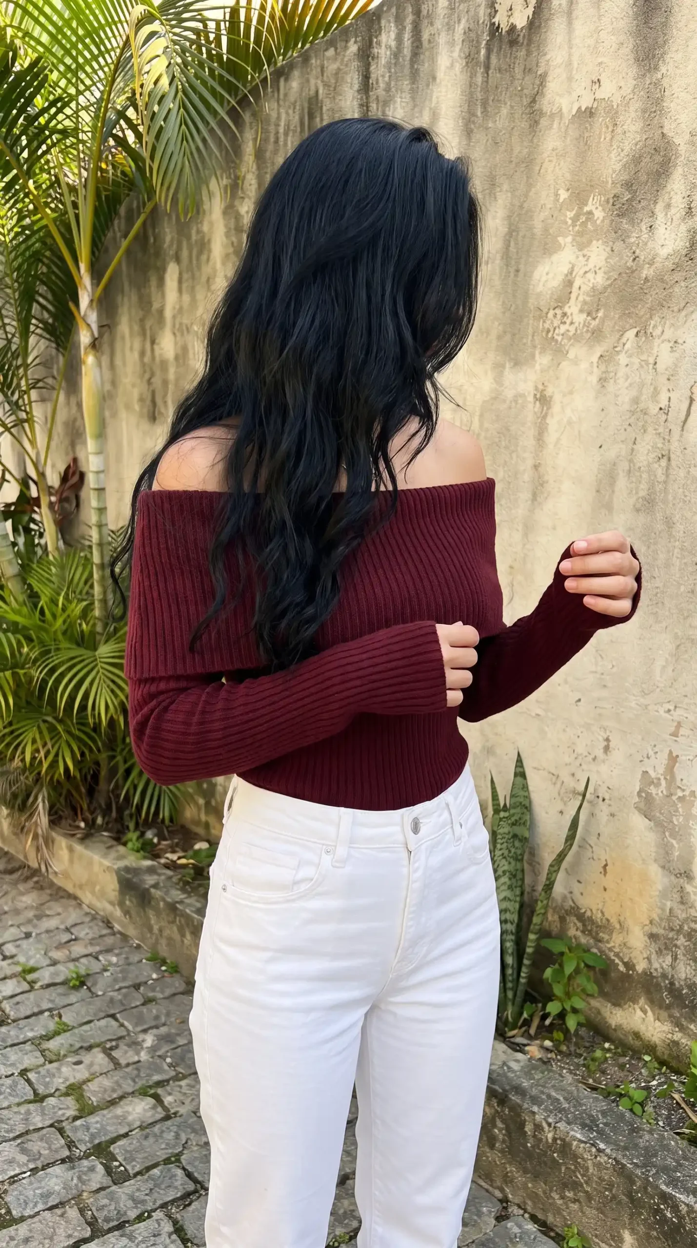Woman wearing burgundy off shoulder ribbed knit top with white straight leg jeans outdoors