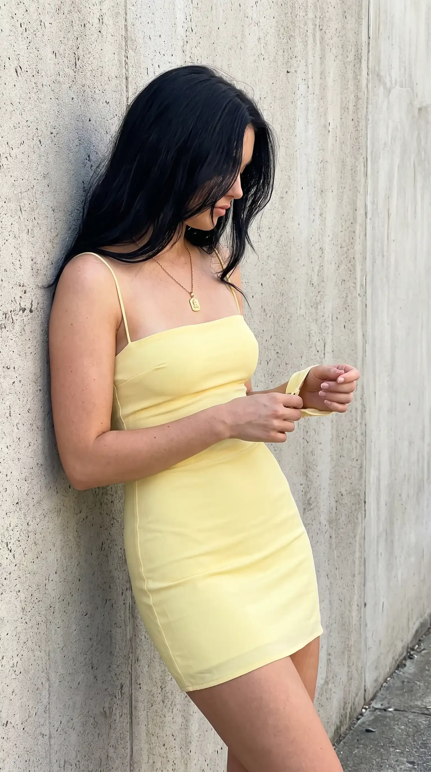 Butter yellow spaghetti strap square neck bodycon mini dress against concrete wall