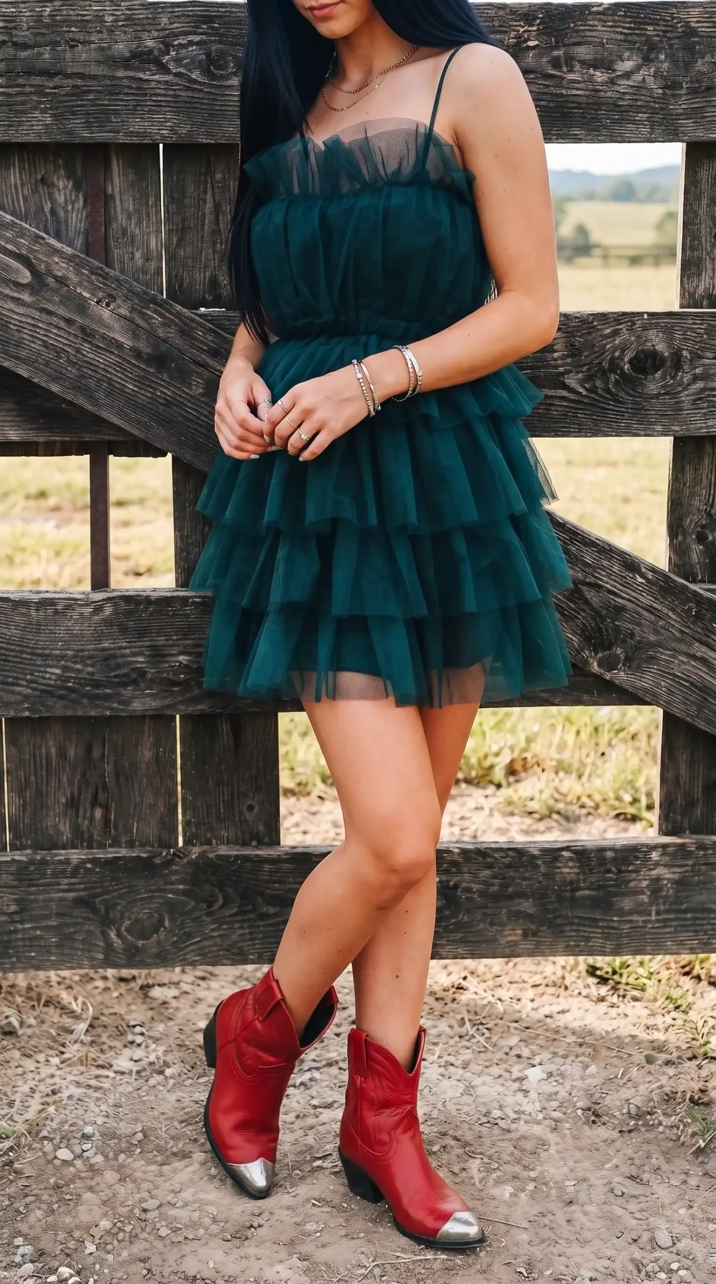 Woman in emerald green tiered tulle mini dress with red cowboy boots near wooden fence