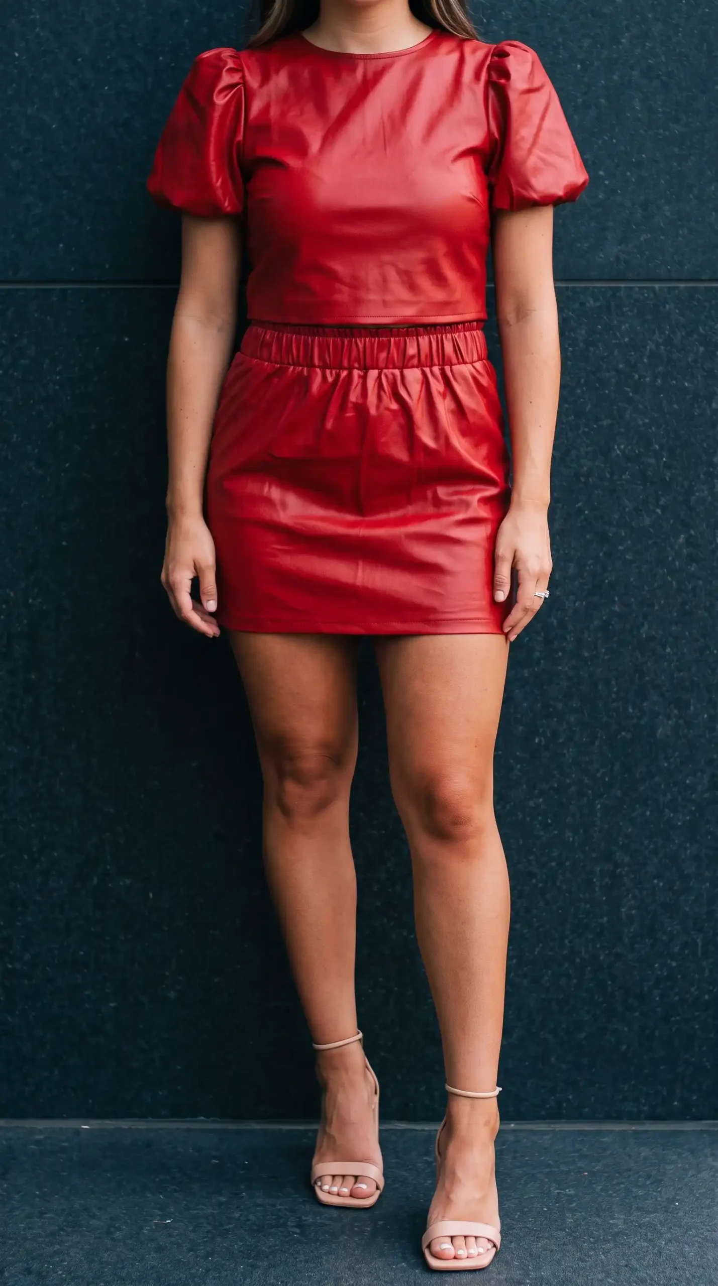 Woman wearing red faux leather puff sleeve crop top and gathered mini skirt with nude heels