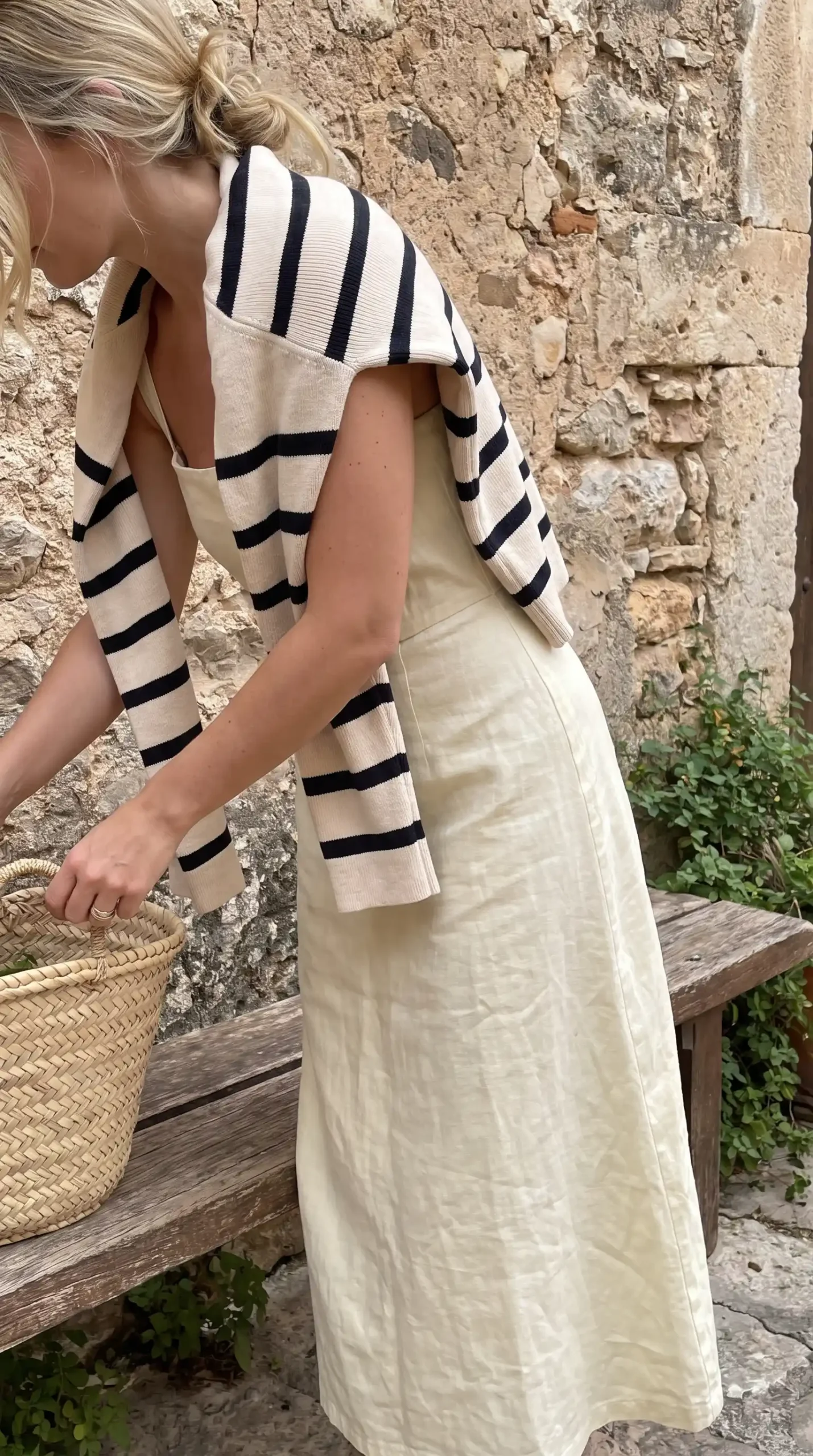 Woman wearing cream linen midi skirt with navy stripe knit draped over shoulders outdoors