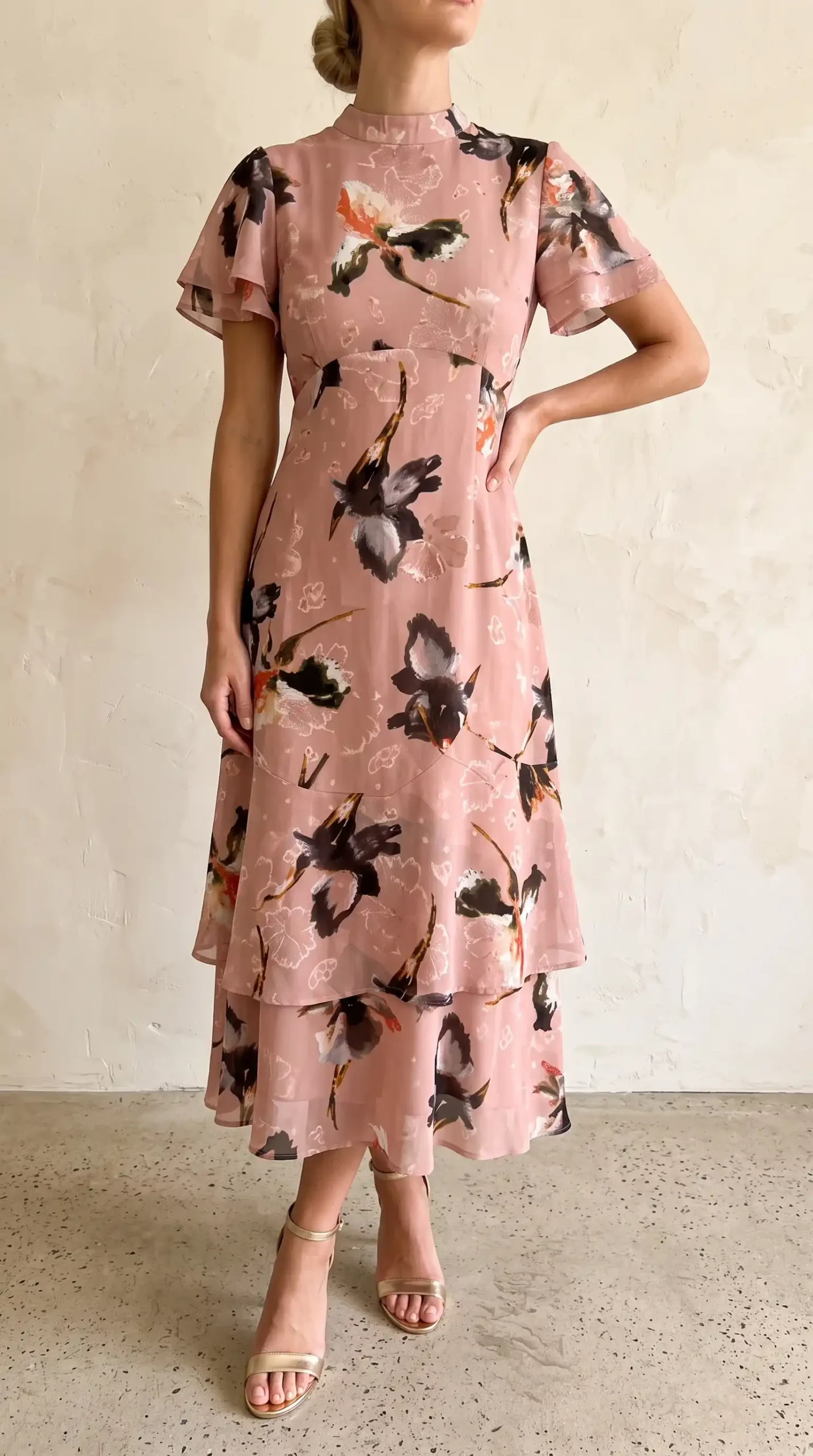 Woman wearing dusty pink bold floral print mock neck flutter sleeve tiered chiffon midi dress
