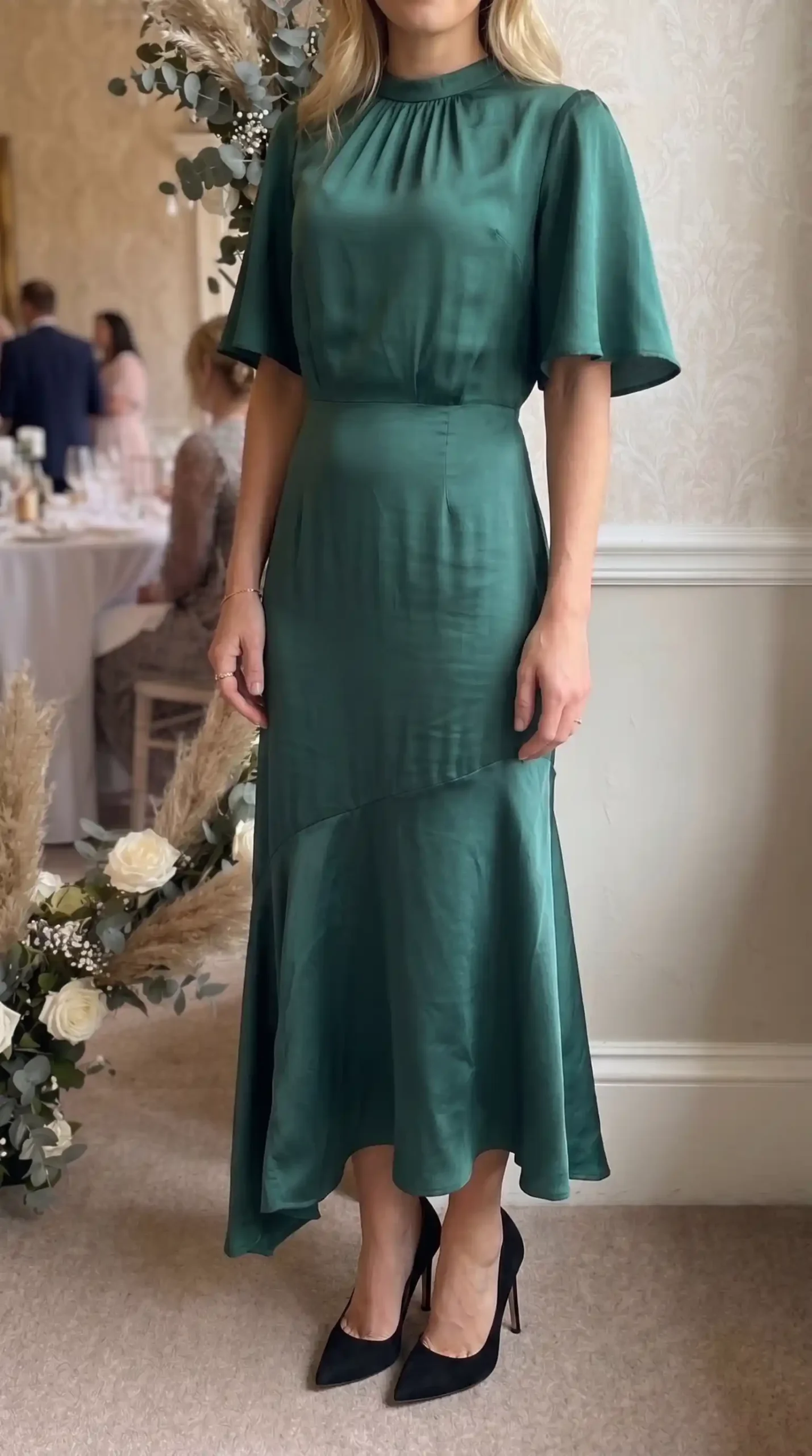 Woman wearing emerald green satin mock neck flutter sleeve asymmetric fishtail maxi dress