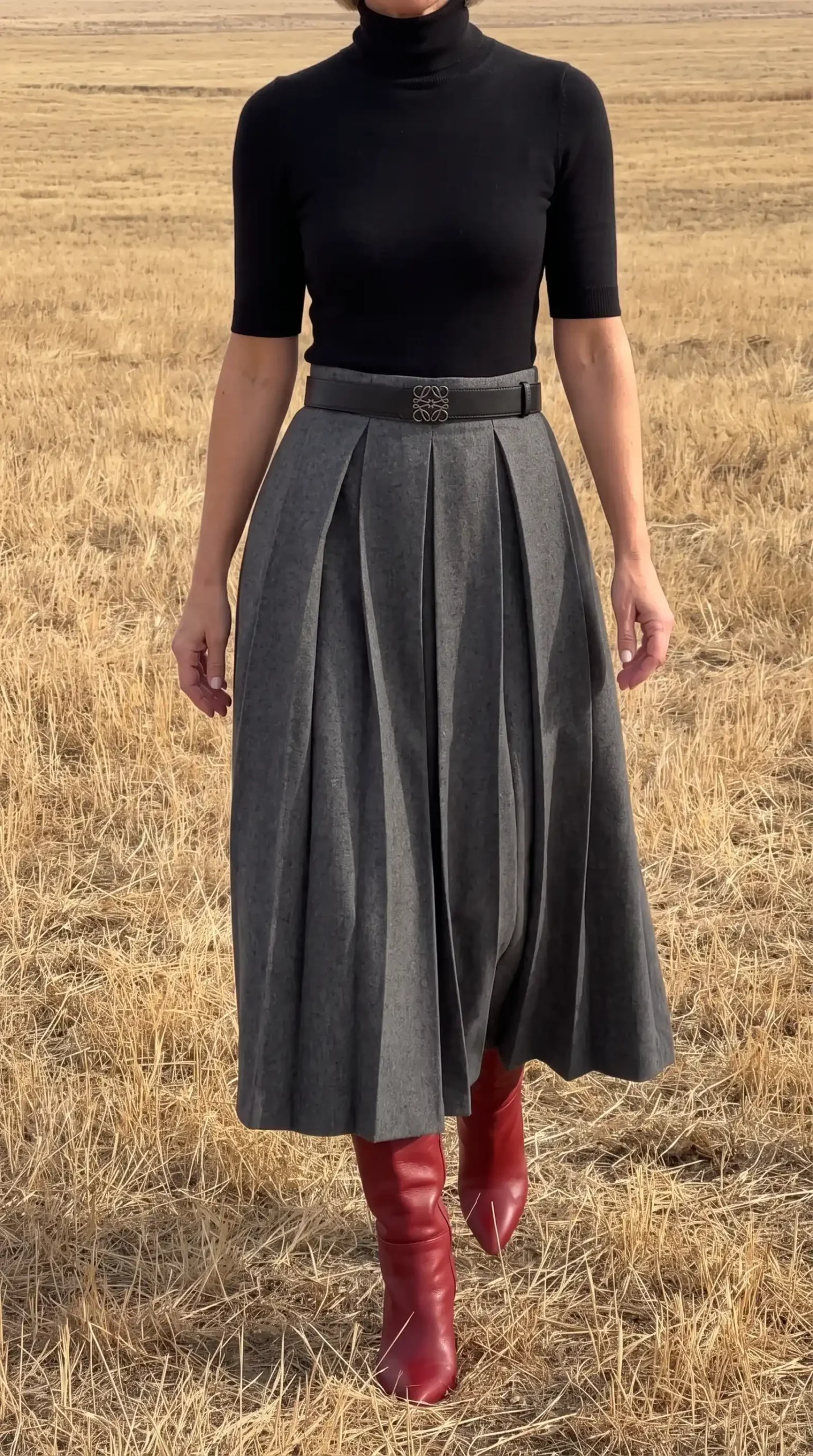 Woman in black short sleeve turtleneck with grey wool pleated midi skirt black belt