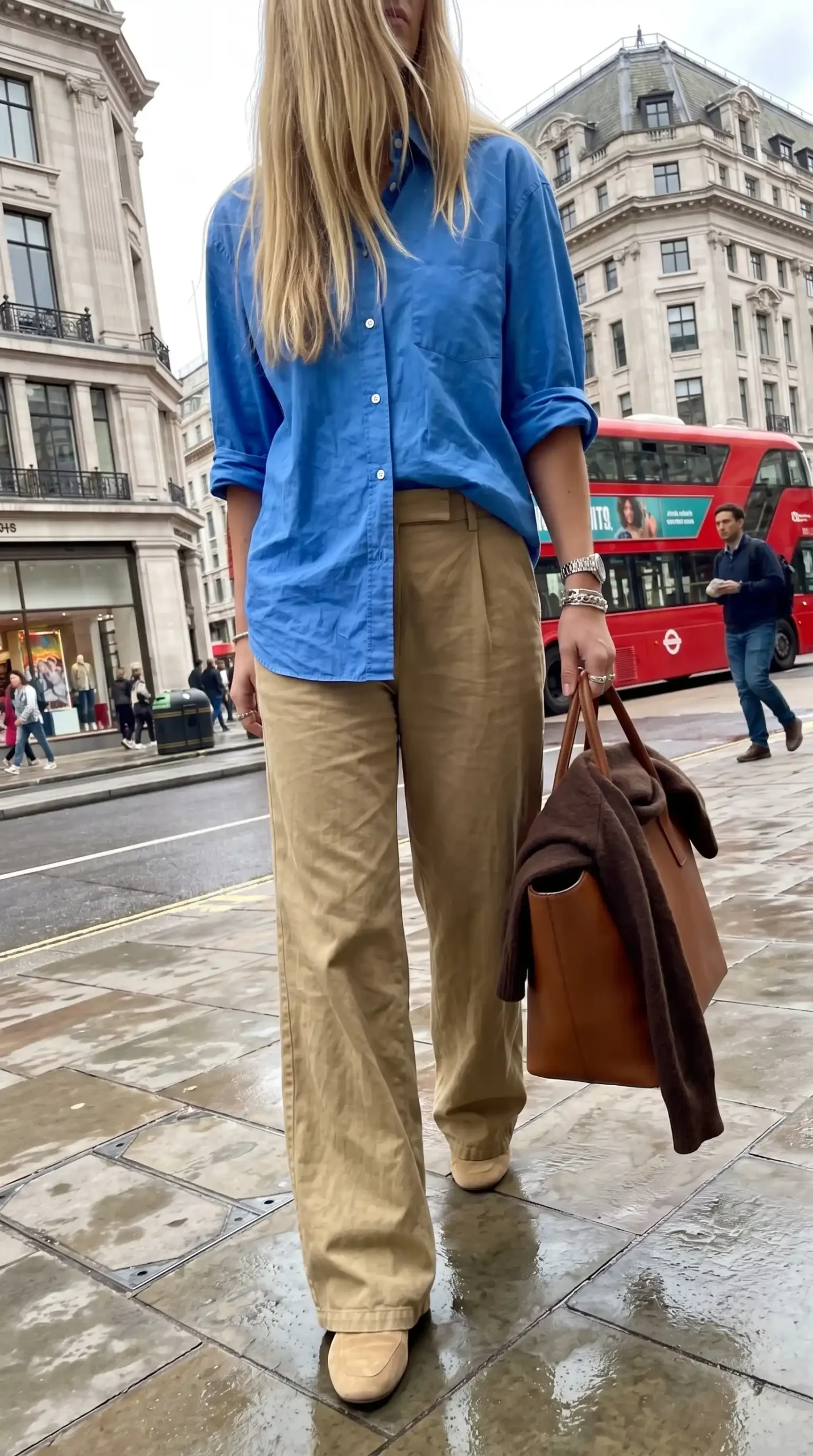 Woman wearing cobalt blue oversized shirt with khaki wide leg trousers tan leather tote and nude ballet flats on wet London street