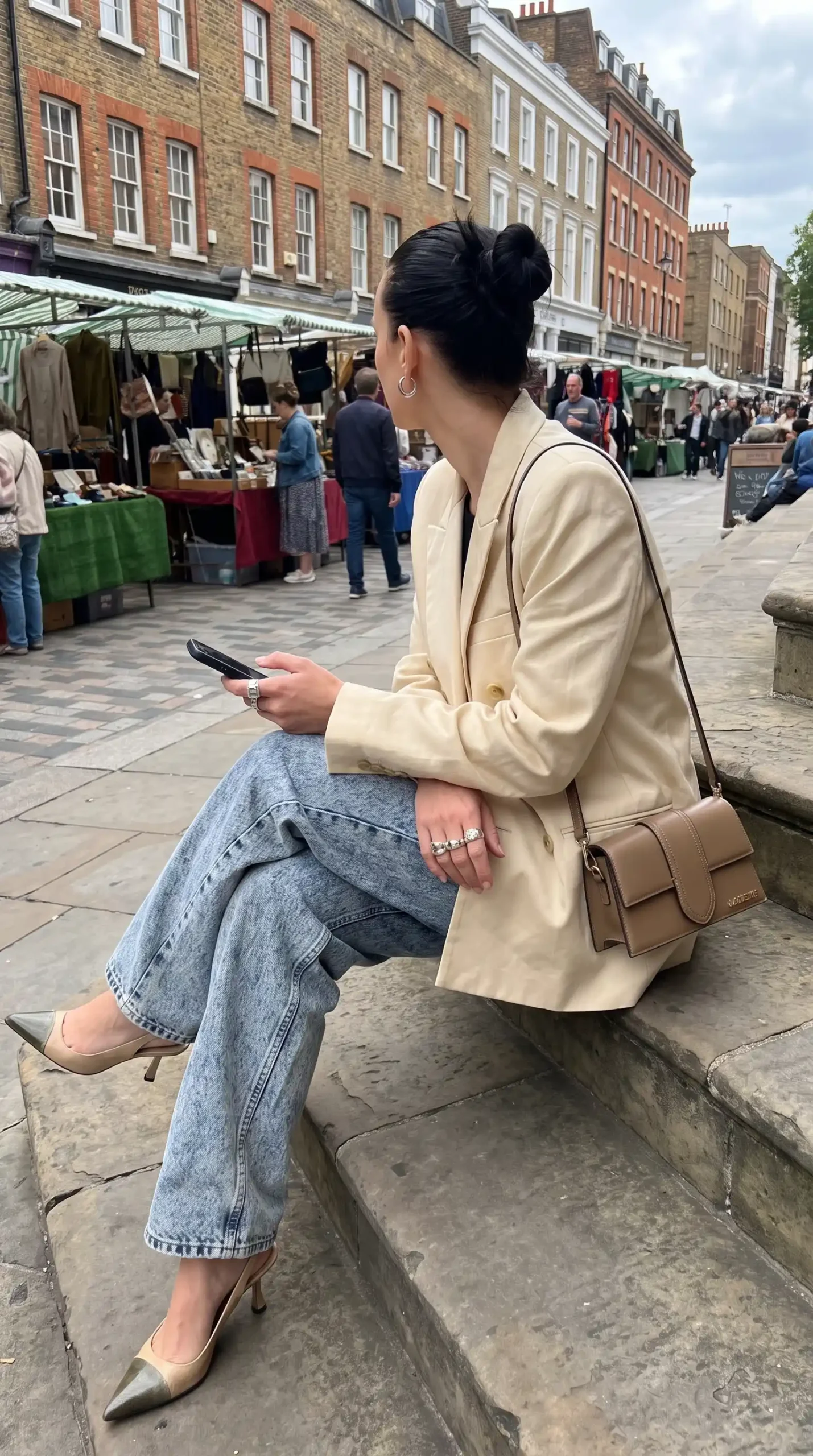 Woman wearing cream oversized blazer with light wash wide leg jeans gold pointed heels and tan crossbody bag at London street market