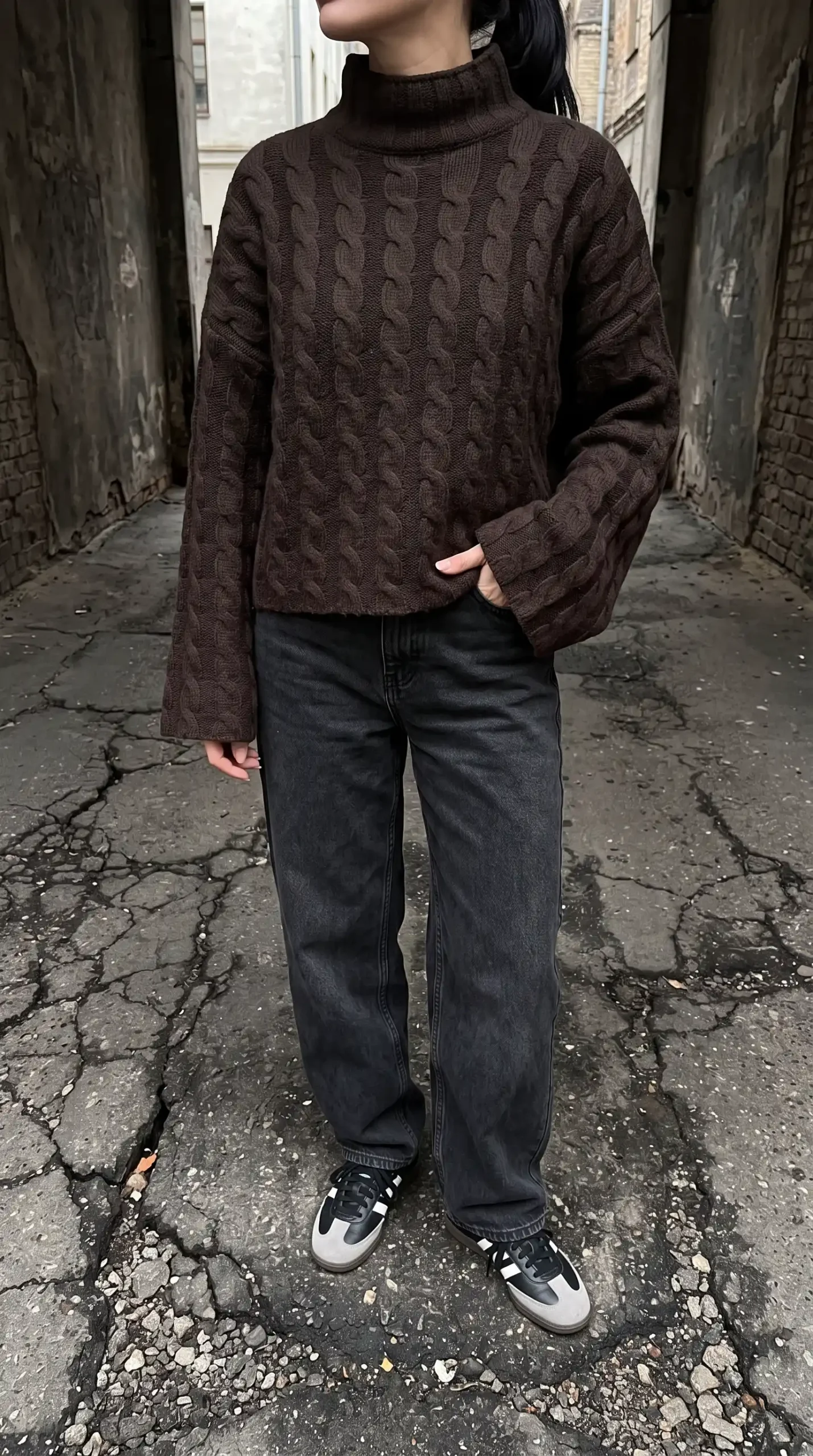 Woman in dark brown cable knit mockneck sweater with black washed wide leg jeans