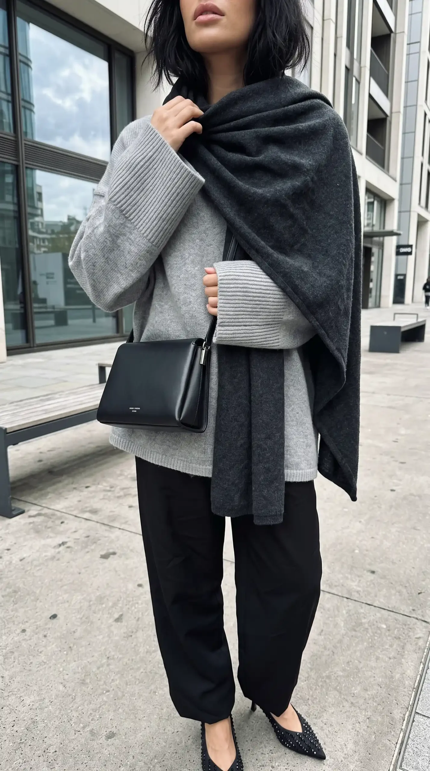 Woman wearing light grey oversized knit sweater with charcoal wool wrap scarf black wide leg trousers and black studded heels outdoors