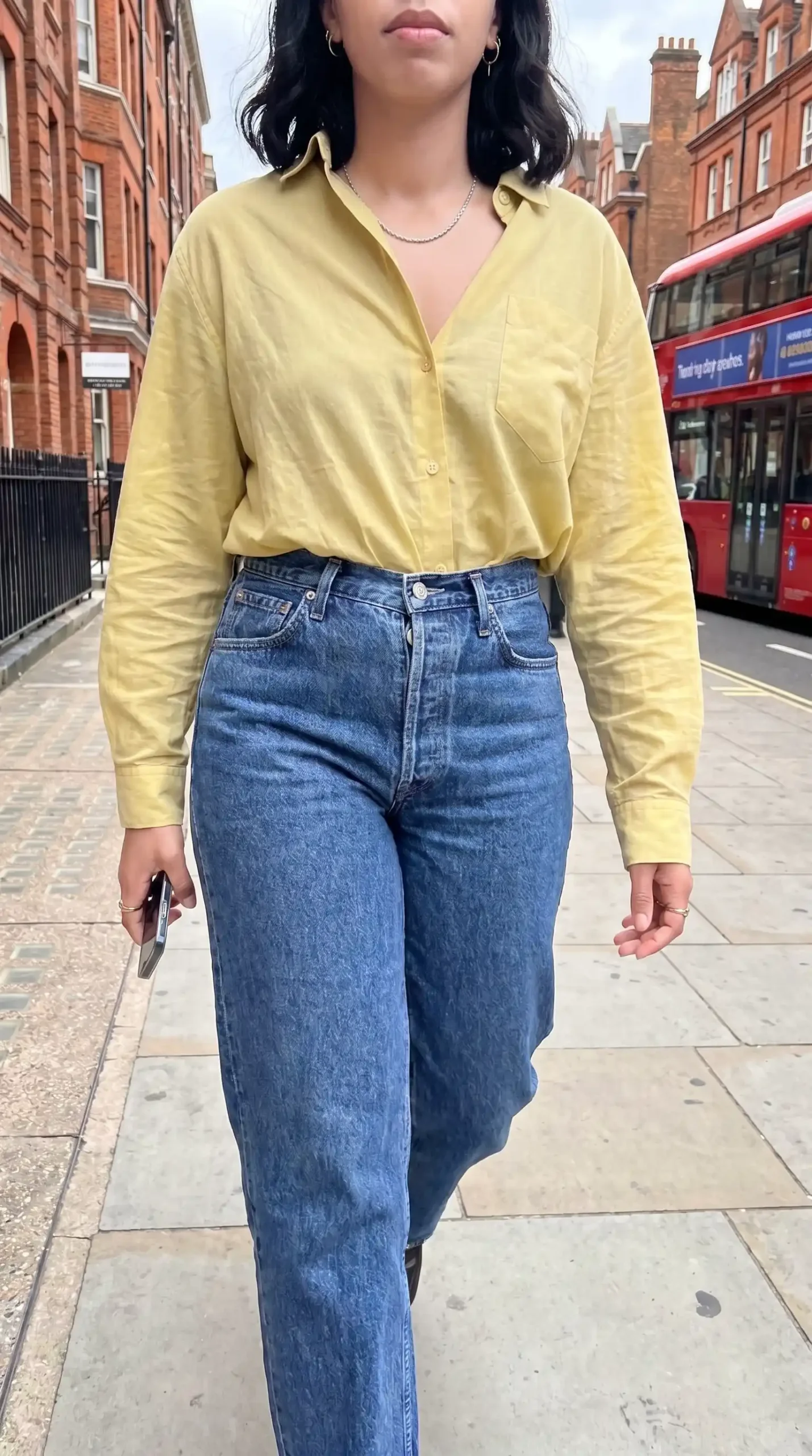 Woman wearing yellow oversized button down shirt with mid wash wide leg jeans on London street