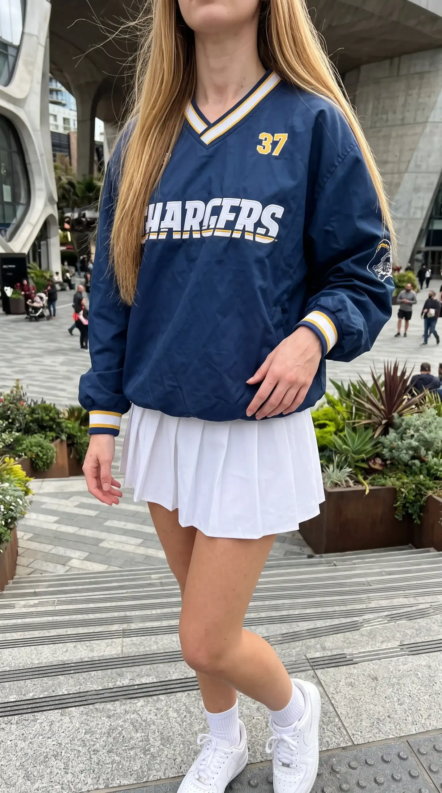 Woman wearing navy blue Chargers pullover windbreaker with white pleated mini skirt and white sneakers outdoors