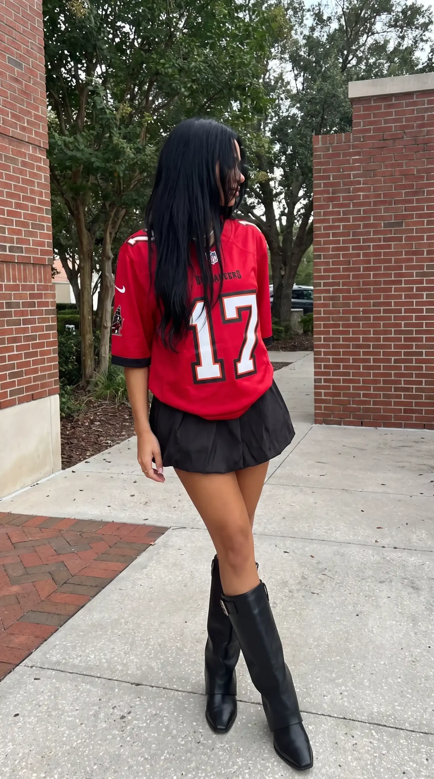 Woman wearing red Buccaneers number 17 jersey with black pleated mini skirt and black knee high boots outdoors