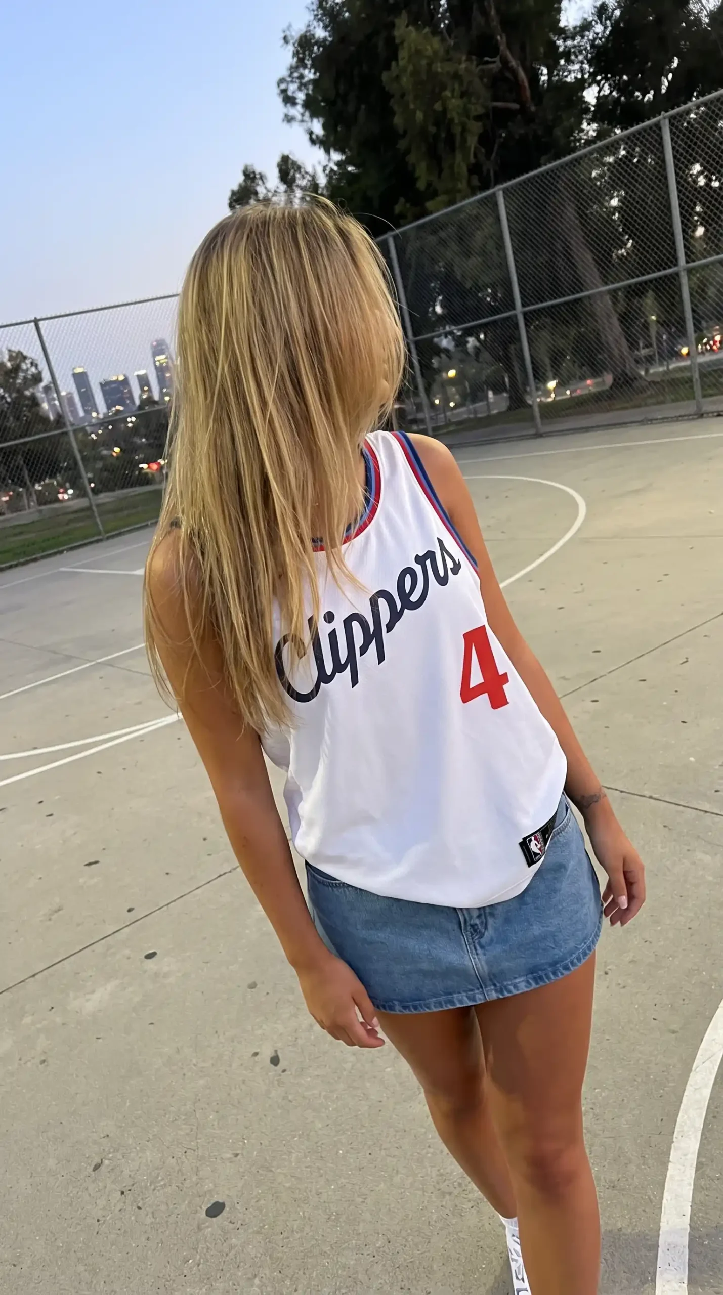 Woman wearing white Clippers basketball jersey with light wash denim mini skirt on basketball court