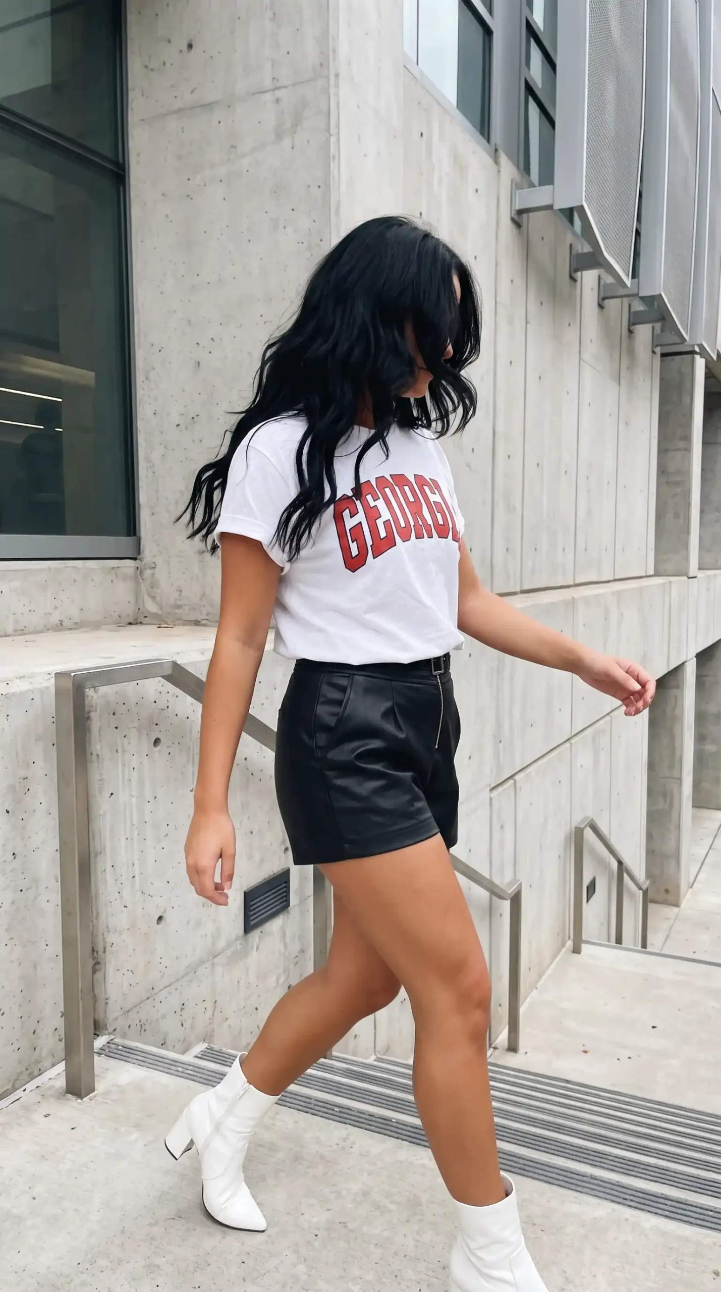 Woman wearing white Georgia graphic tee with black faux leather mini skirt and white ankle boots outdoors