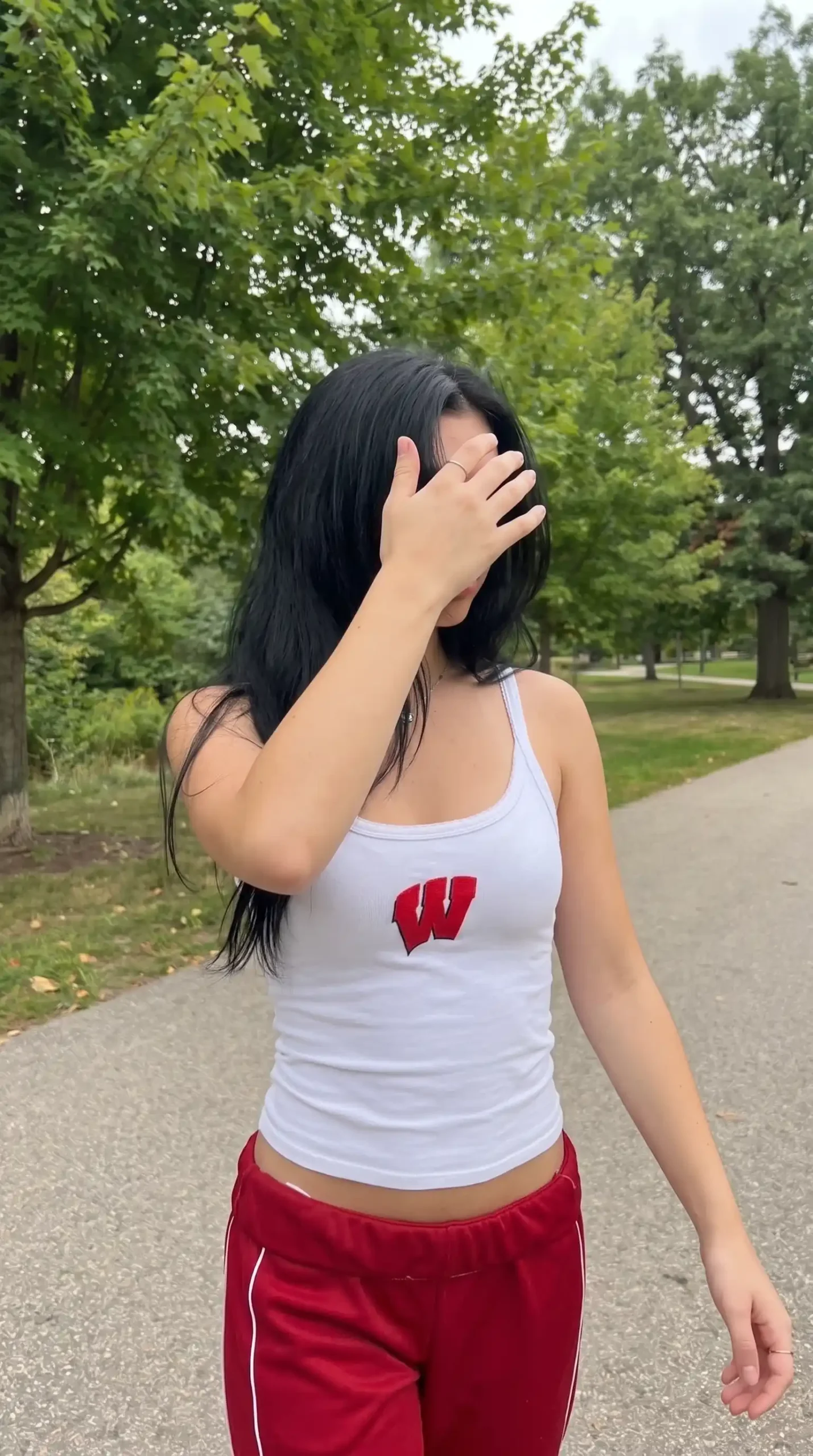 Woman wearing white Wisconsin W graphic tank with red track pants in park