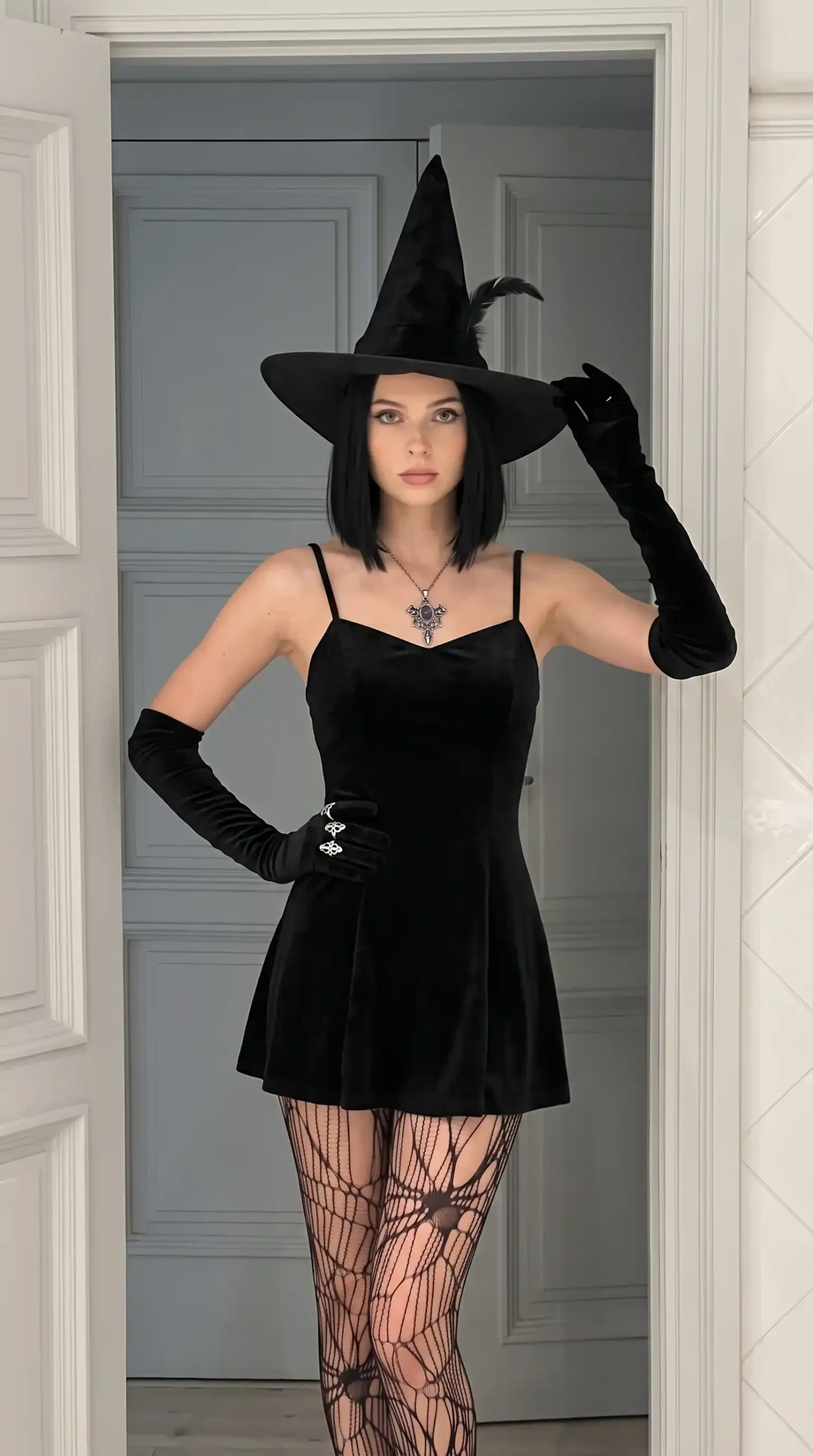 Woman wearing black velvet witch Halloween costume with spiderweb tights, elbow gloves and pointed hat