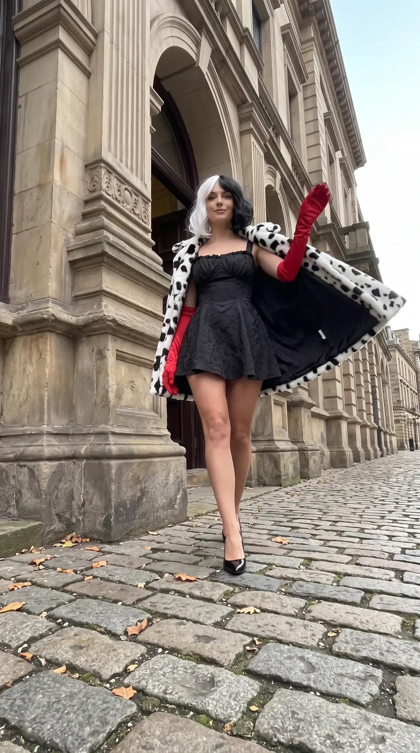 Woman dressed as Cruella de Vil in dalmatian faux fur coat black corset mini dress red gloves and black heels