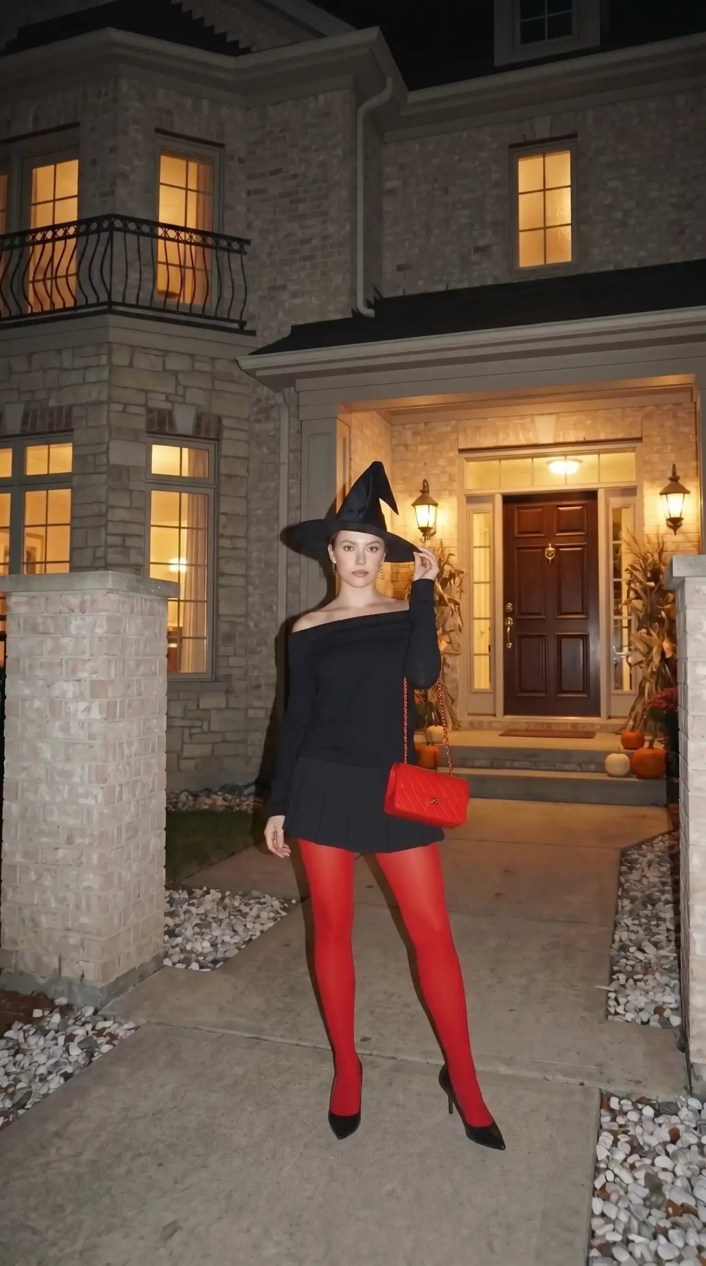 Woman wearing glamorous witch Halloween costume with black off-shoulder mini dress red tights and pointed hat