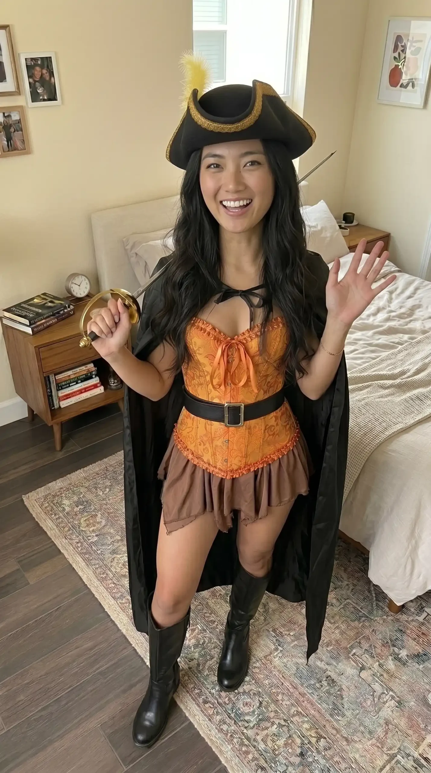 Woman dressed as pirate captain in orange brocade corset dress black cape tricorn hat and tall black boots